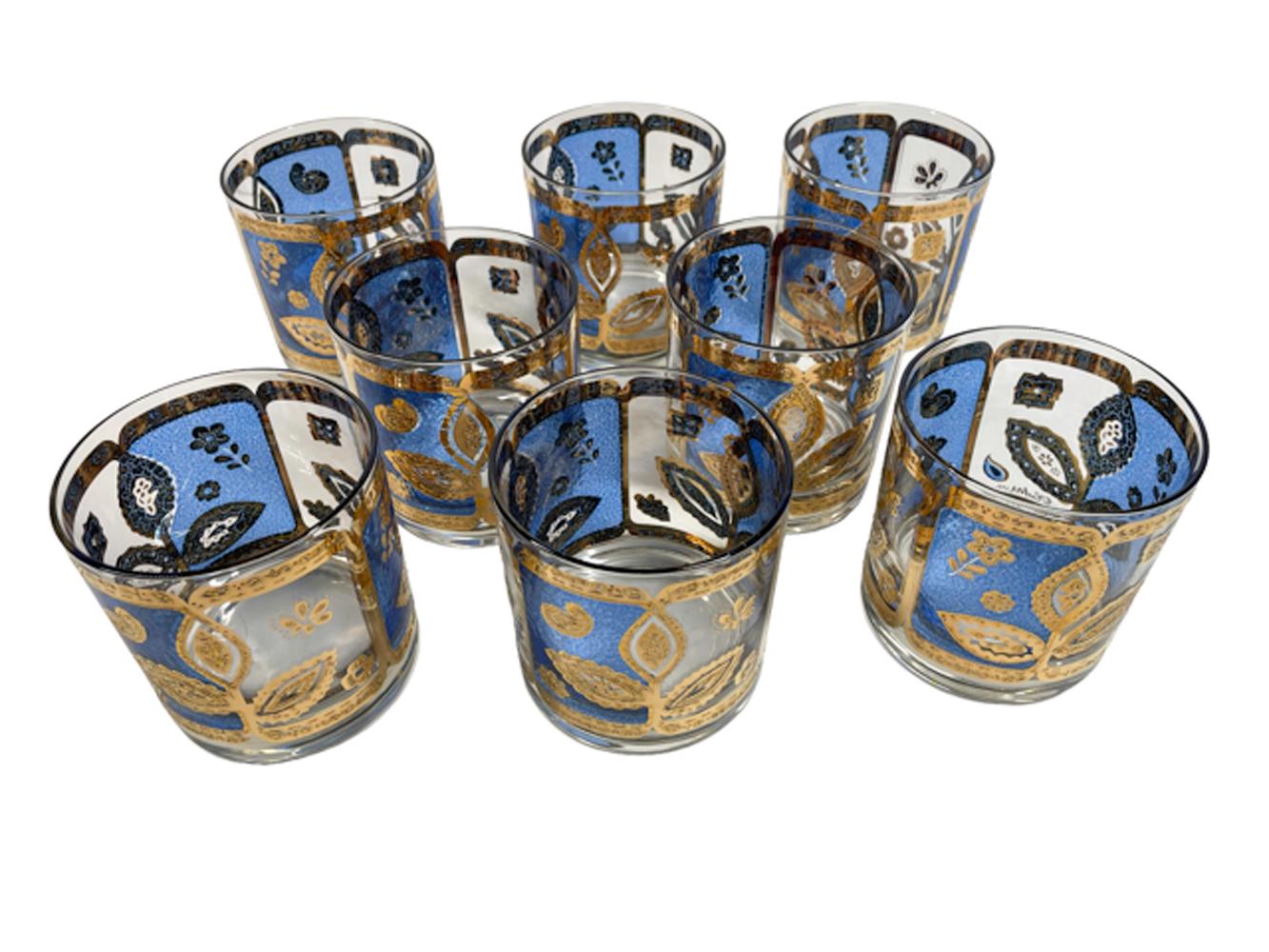 Set of eight hard to find Culver rocks glasses in translucent blue enamel with raised, textured 22 karat gold. Each with three panels framed in gold and split into blue and clear halves centering a trio of leaves. Signed Culver LTD and with a wood