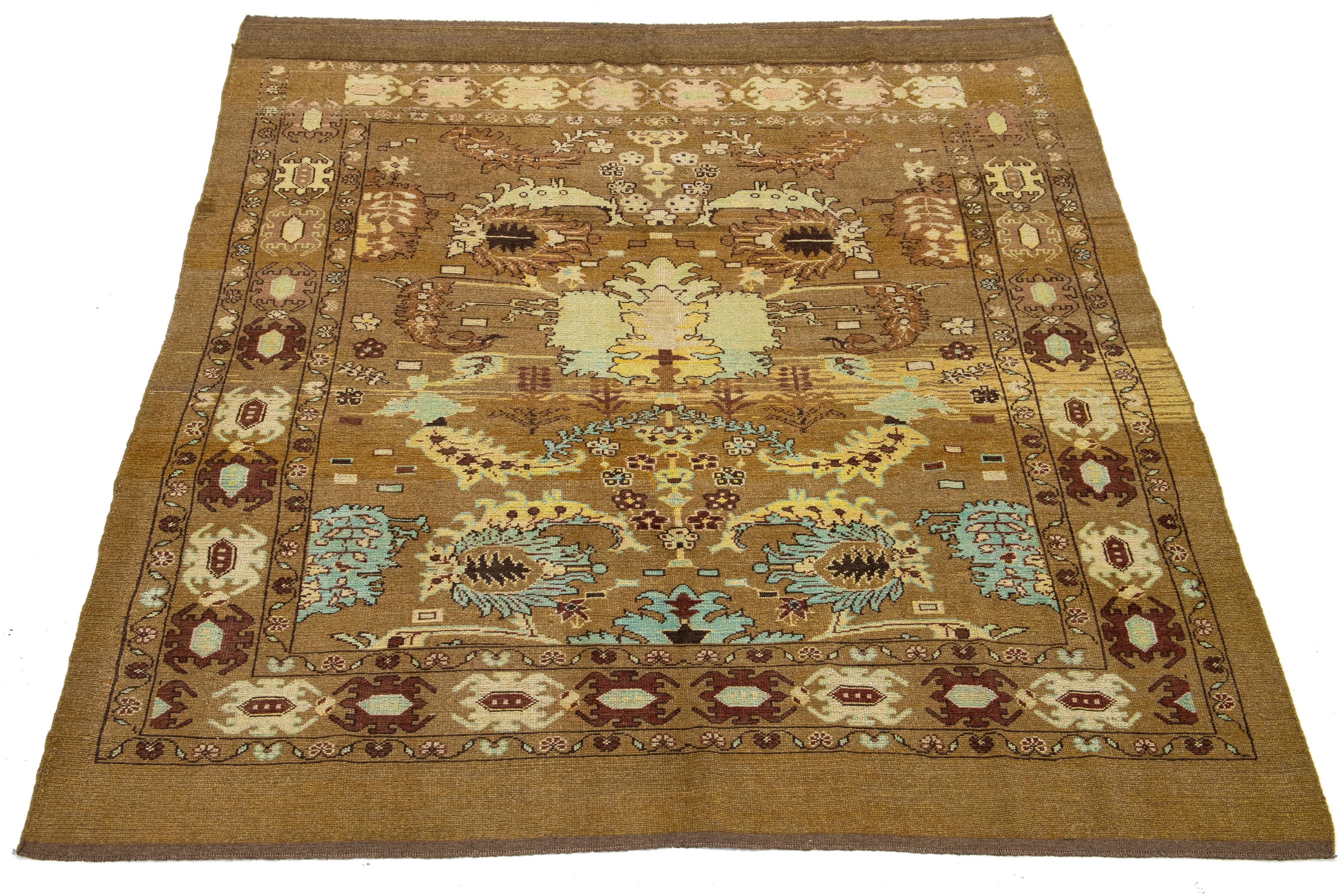 This beautiful, room-sized modern rug is hand-knotted from wool and has a brown and yellow base. It is part of Apadana's Revival Collection and features blue, beige, and brick-red accents alongside a stunning geometric botanical floral design.

This