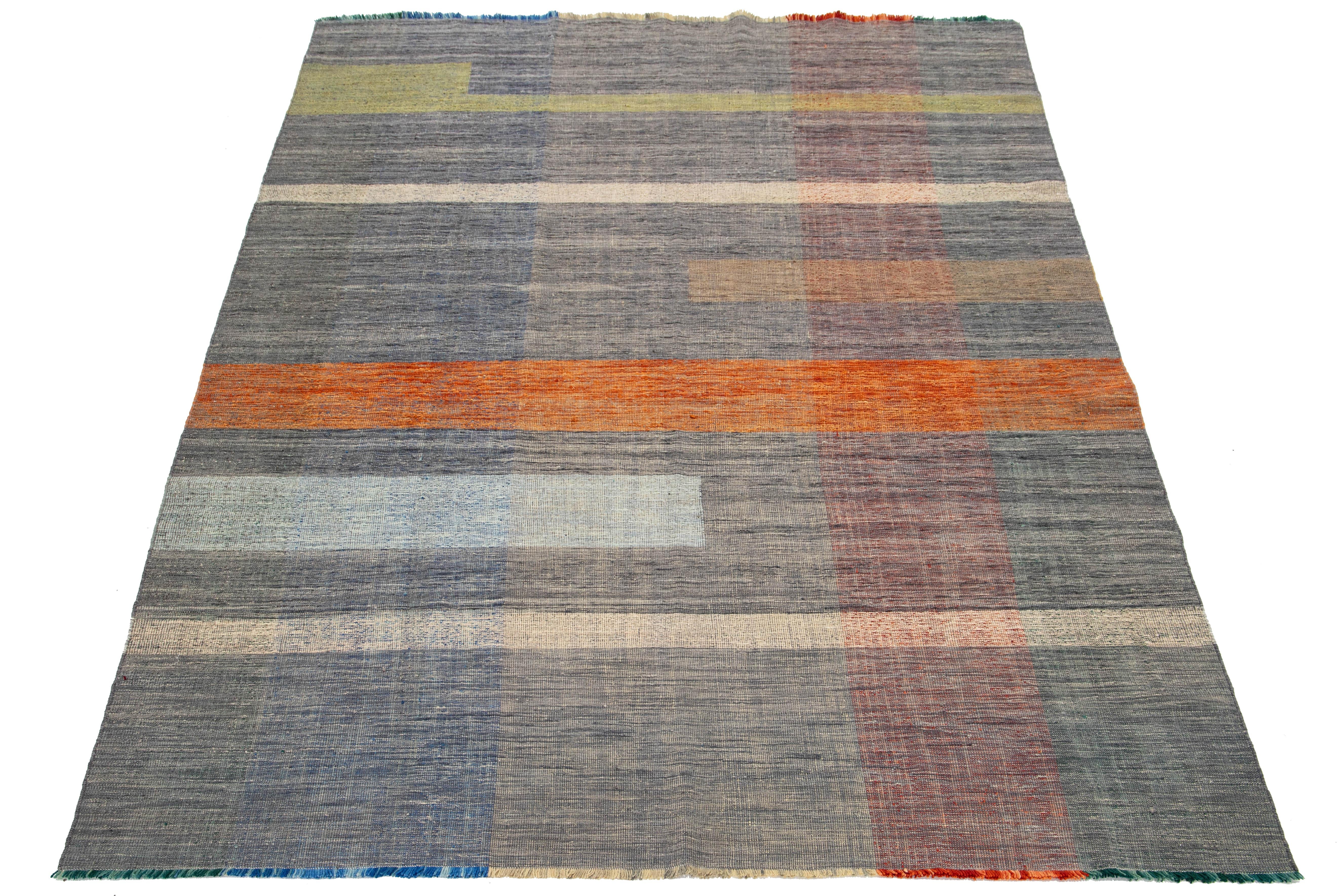 This rug showcases an organic modern design with a wool Kilim flatweave, featuring a geometric pattern in vibrant hues of gray, orange, green, blue, and pink.

This rug measures 8'5