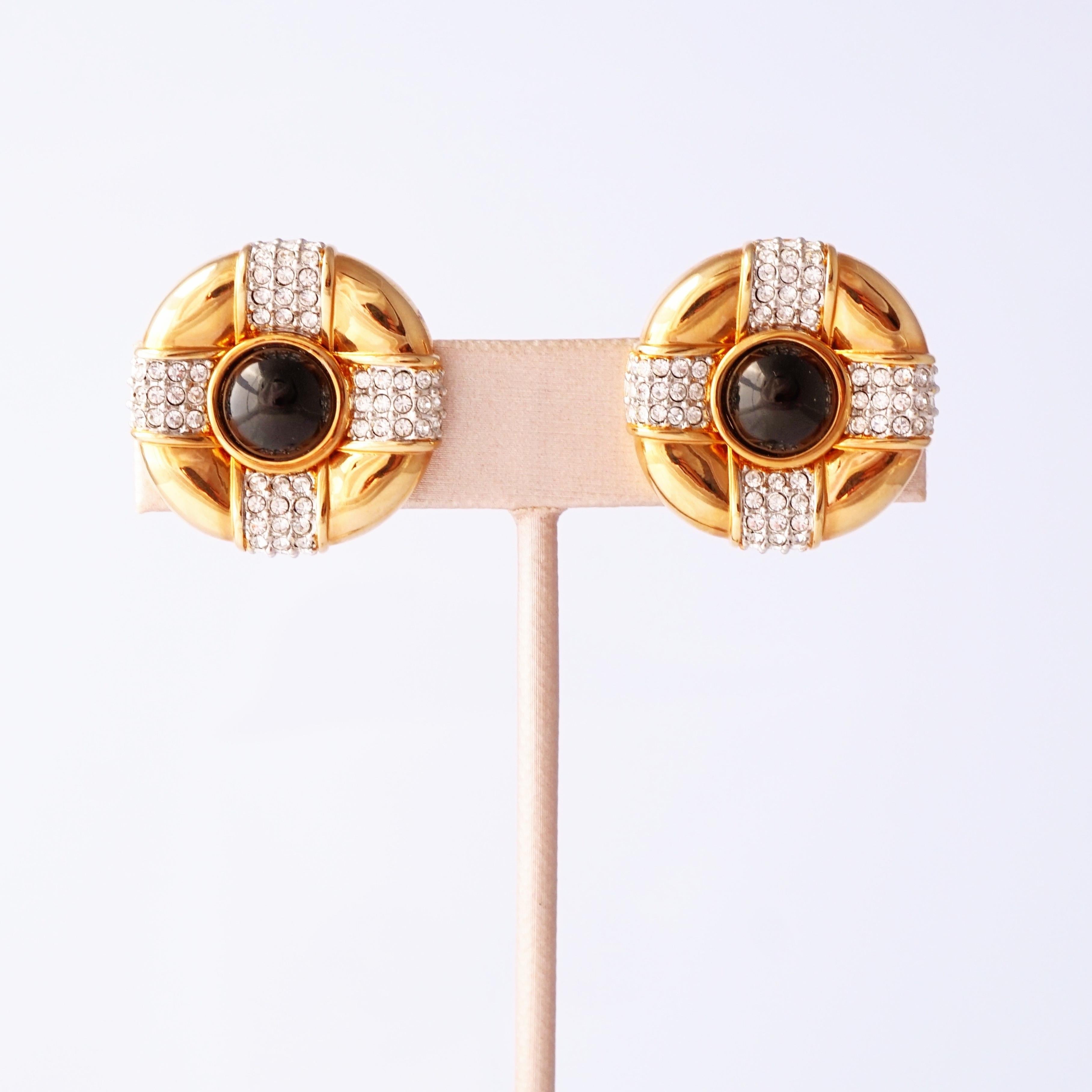 Radiosi e raffinati, questi orecchini Swarovski degli anni '80 regalano pura opulenza vintage. Realizzati in metallo dorato, presentano cabochon in vetro onice nero lucido al centro, incorniciati da scintillanti cristalli incastonati che catturano