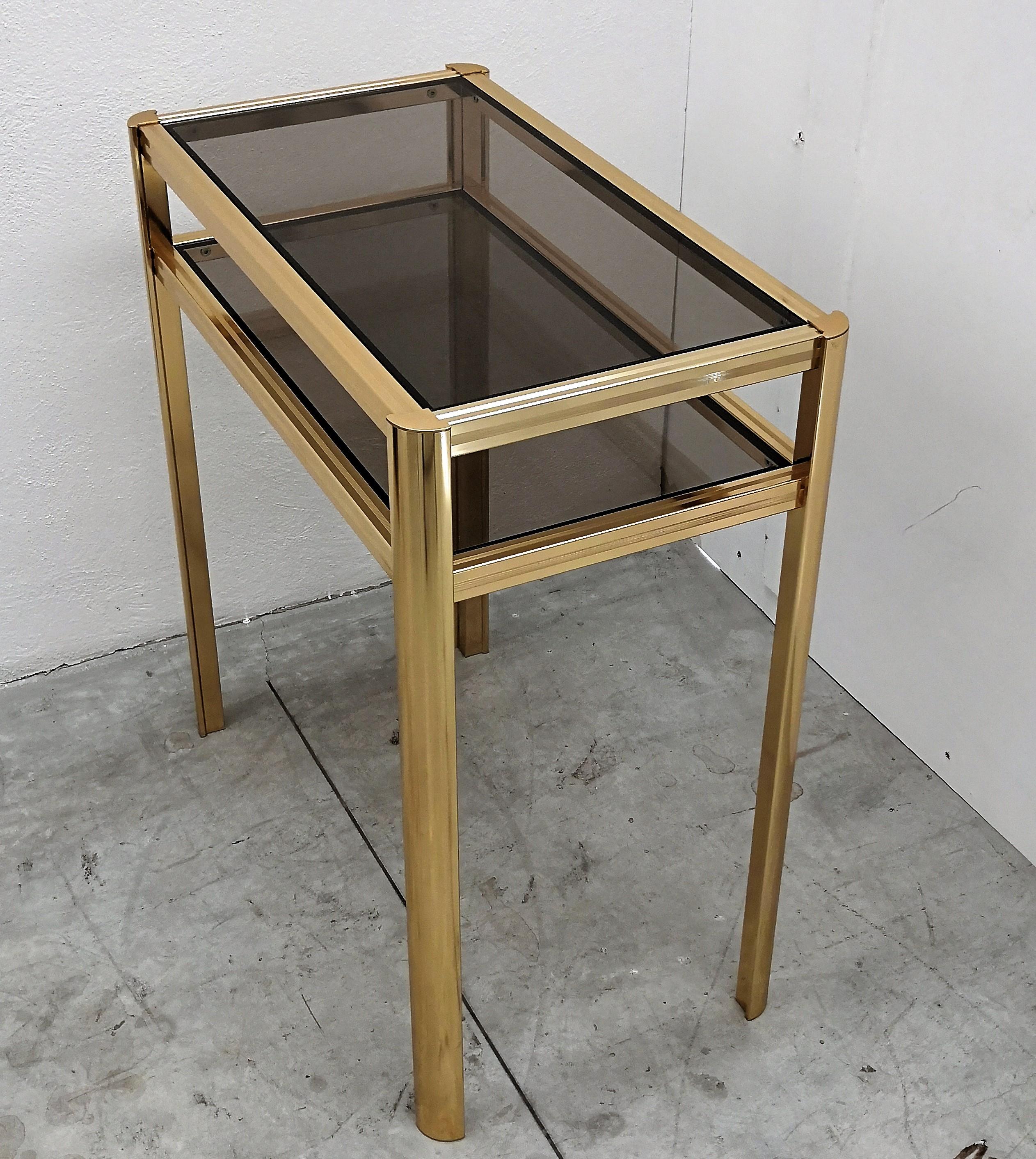 Beautiful and stylish vintage 1980s Italian brass console with two smoked glass shelves. 
A great piece that perfectly adds to every home decor the typical glitz, glamour and gold of Hollywood Regency style, with a nod to Art Deco decadence and
