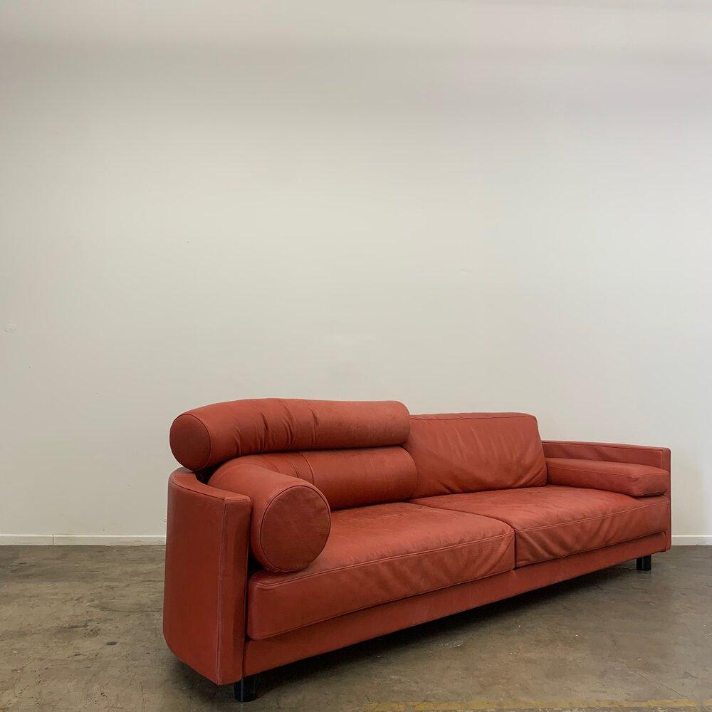 This 80s sofa offers optimal comfort without sacrificing design. Provides ample back support on either side; standard cushion and tubular cushion. Varying arm rests include; one angular cushion and one tubular. Vibrant red leather contrasts well