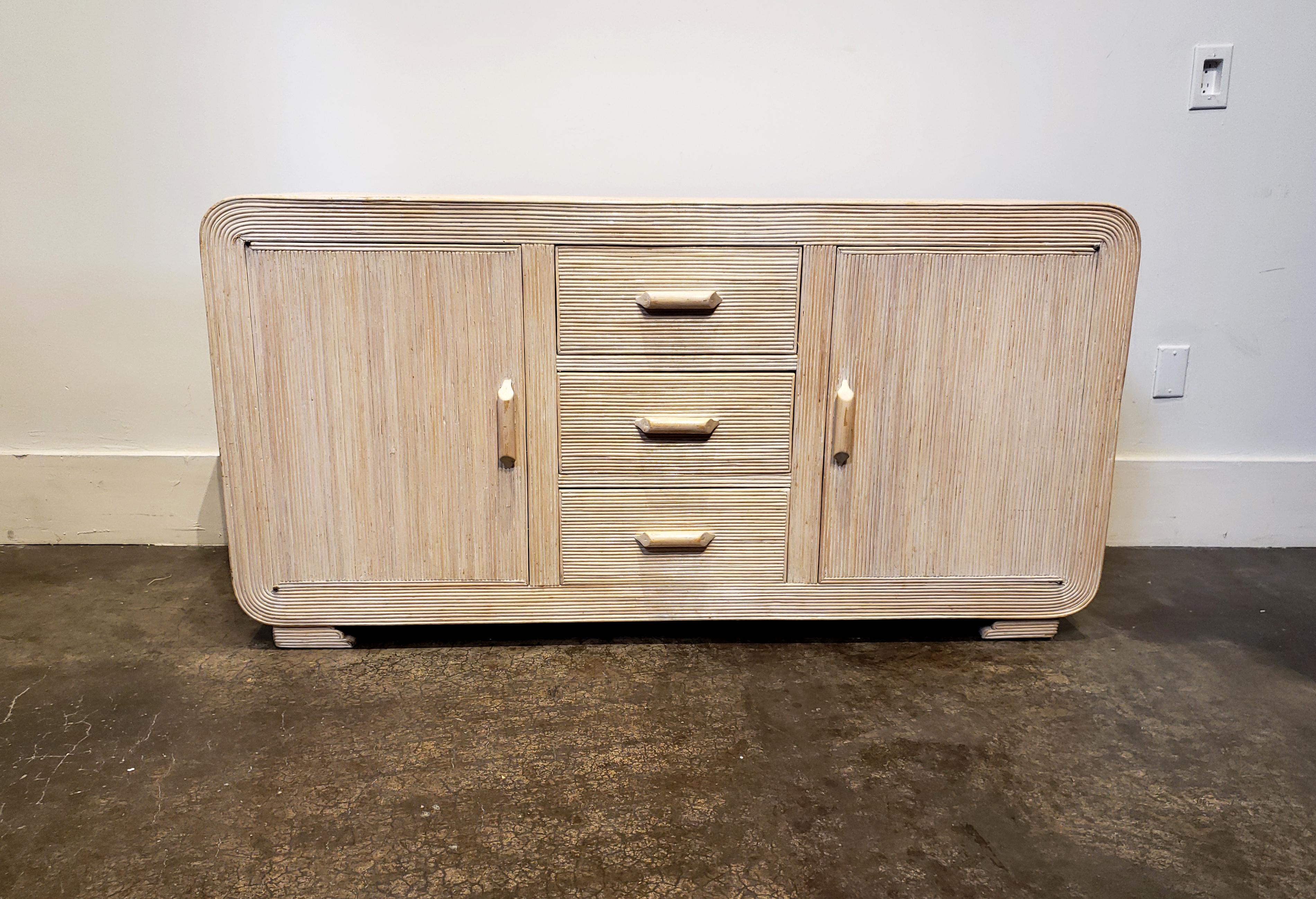 Lovely little whitewashed rattan credenza or sideboard with circular pattern to top that radiates out and down the sides. Has two side cabinet doors with whitewashed interiors and three stacked central drawers. A Classic 1980s piece that fits in