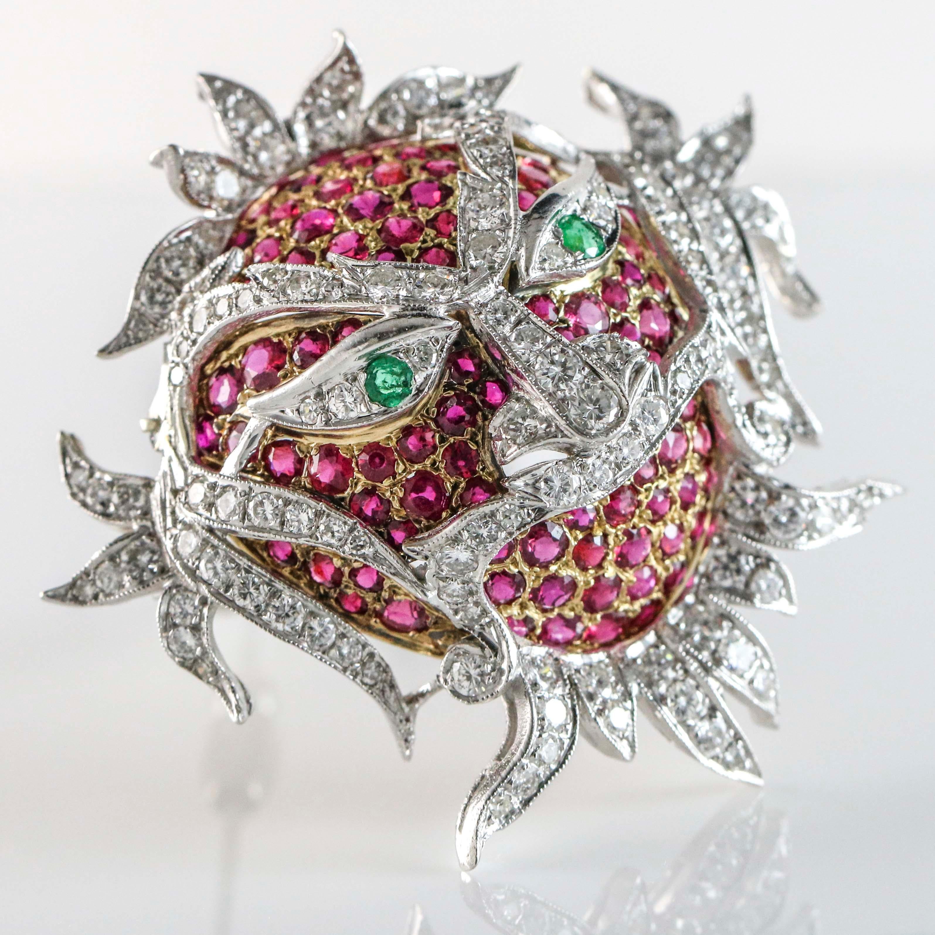 Carnival ornate mask pin crafted in 18k white and yellow gold with emerald eyes. The brooch is prong set with 95 natural round cut rubies, and 135 round brilliant cut diamonds. Ruby total carat weight, 5 carats. Diamond total carat weight, 3 carats.