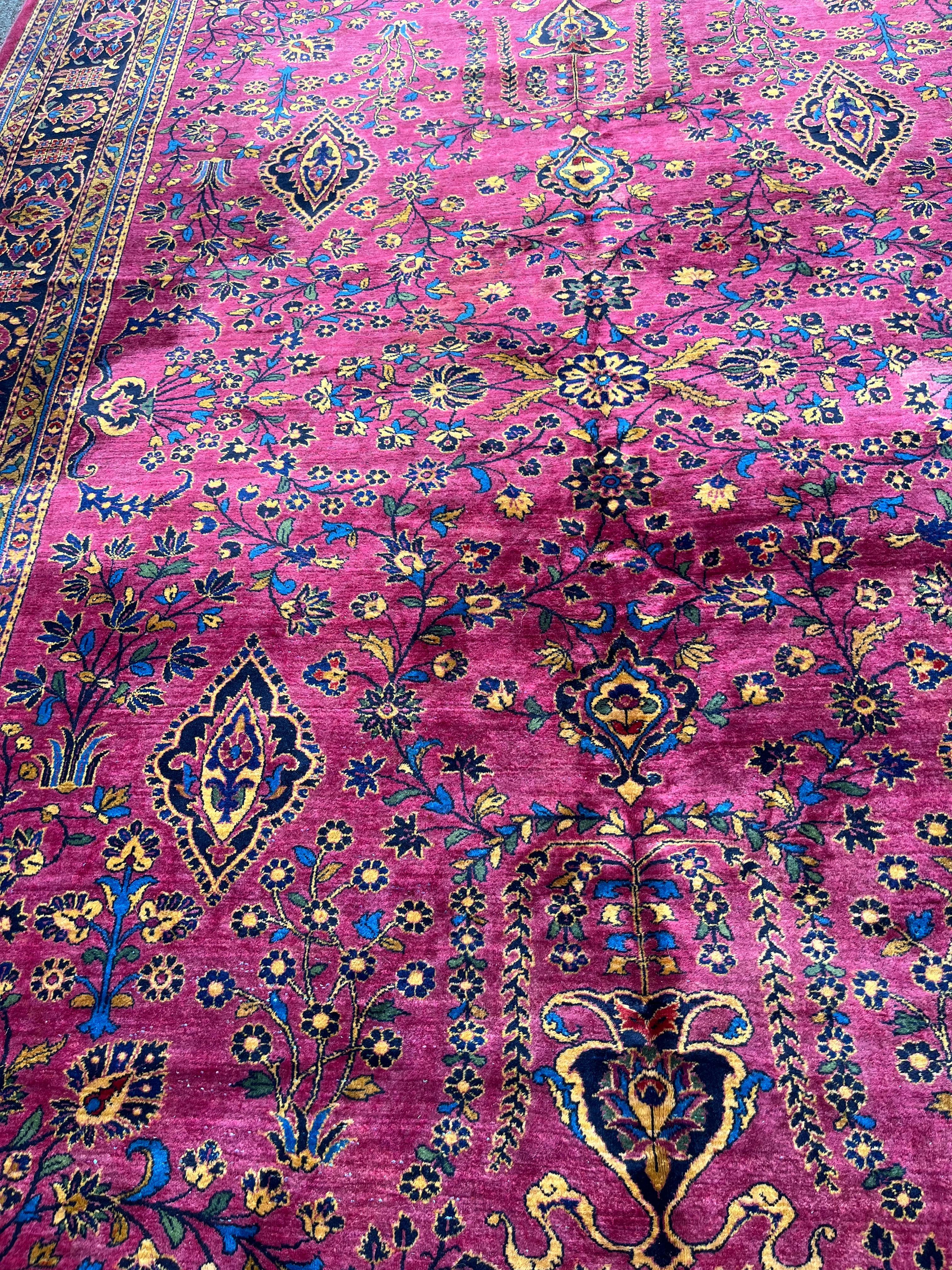 This roomsize, handknotted, antique, wool carpet from India has a striking wine field color and floral designs in rich complementary colors radiating an overall jewel tone. It was made in the famous Tuftanjian workshop in India. Tuftanjian emigrated