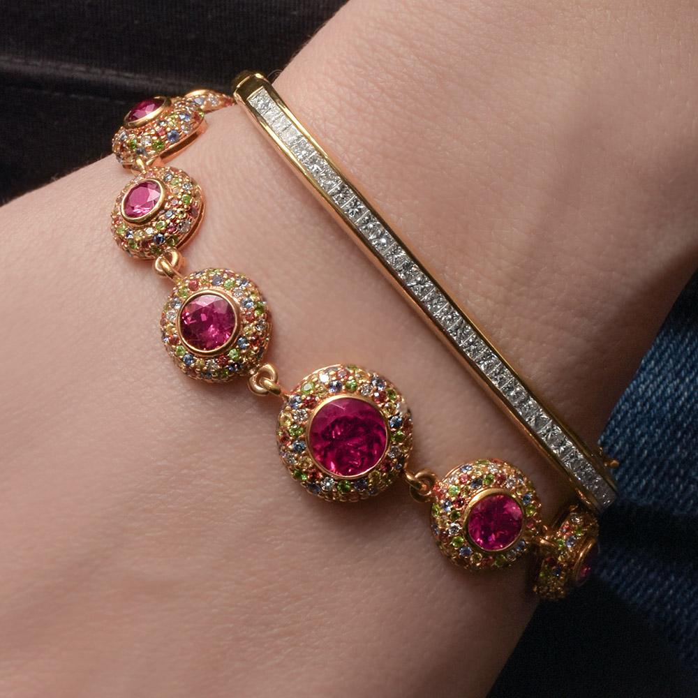 18 Karat Rose Gold graduated round cut Rubellite bracelet surrounded by multi color sapphires and diamonds. 
34.60 grams of gold. 
8.11 carats of multi color sapphires
9.20 carats of Rubellite 
1.25 carats of Diamonds. 
Appraisal Upon request.