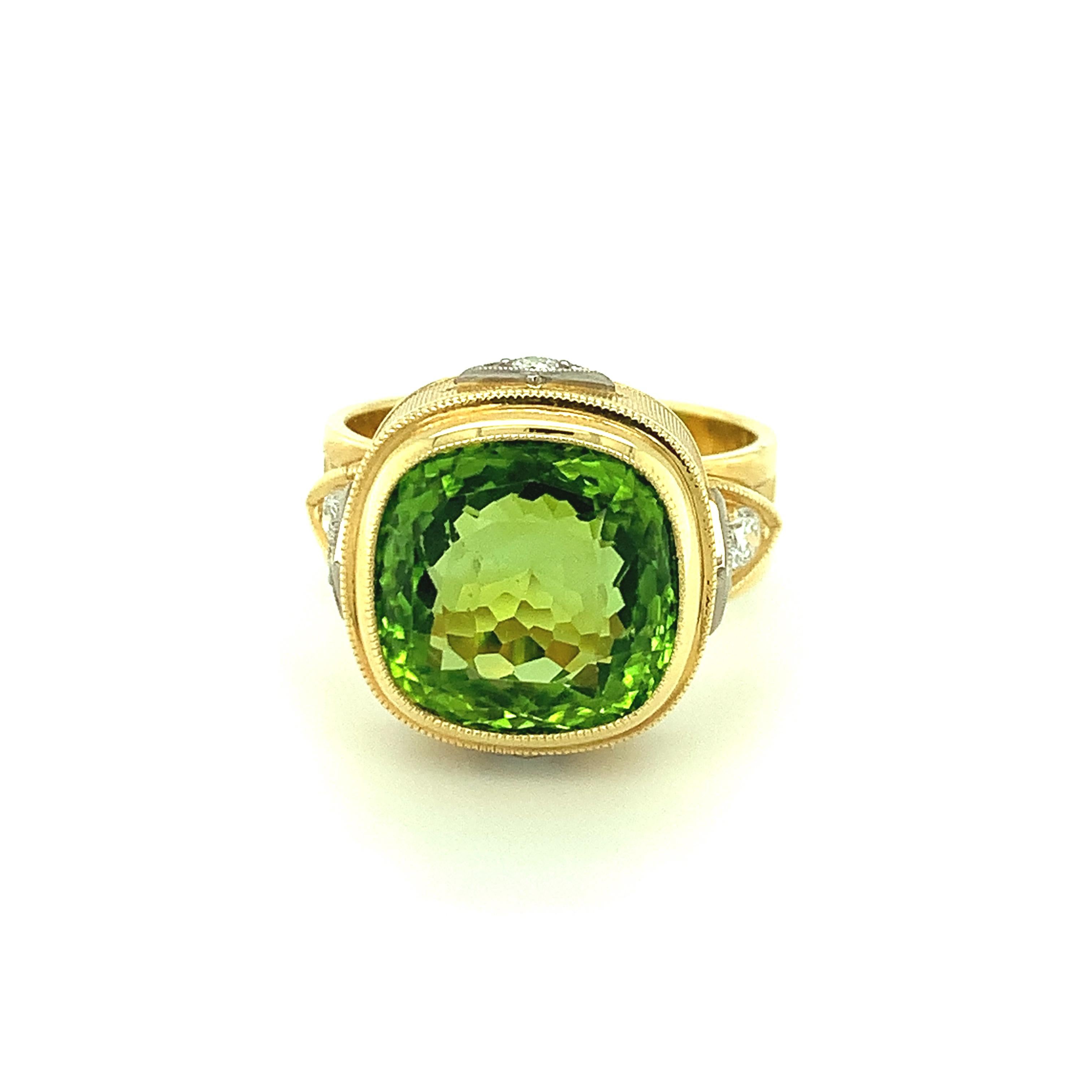 This handsome 18k gold ring features a beautifully crystalline, 8.15 carat cushion-cut peridot with gorgeous, bright green color. Four sparkling, brilliant cut white diamonds set in 18k white gold adorn the finely engraved bezel, with an additional