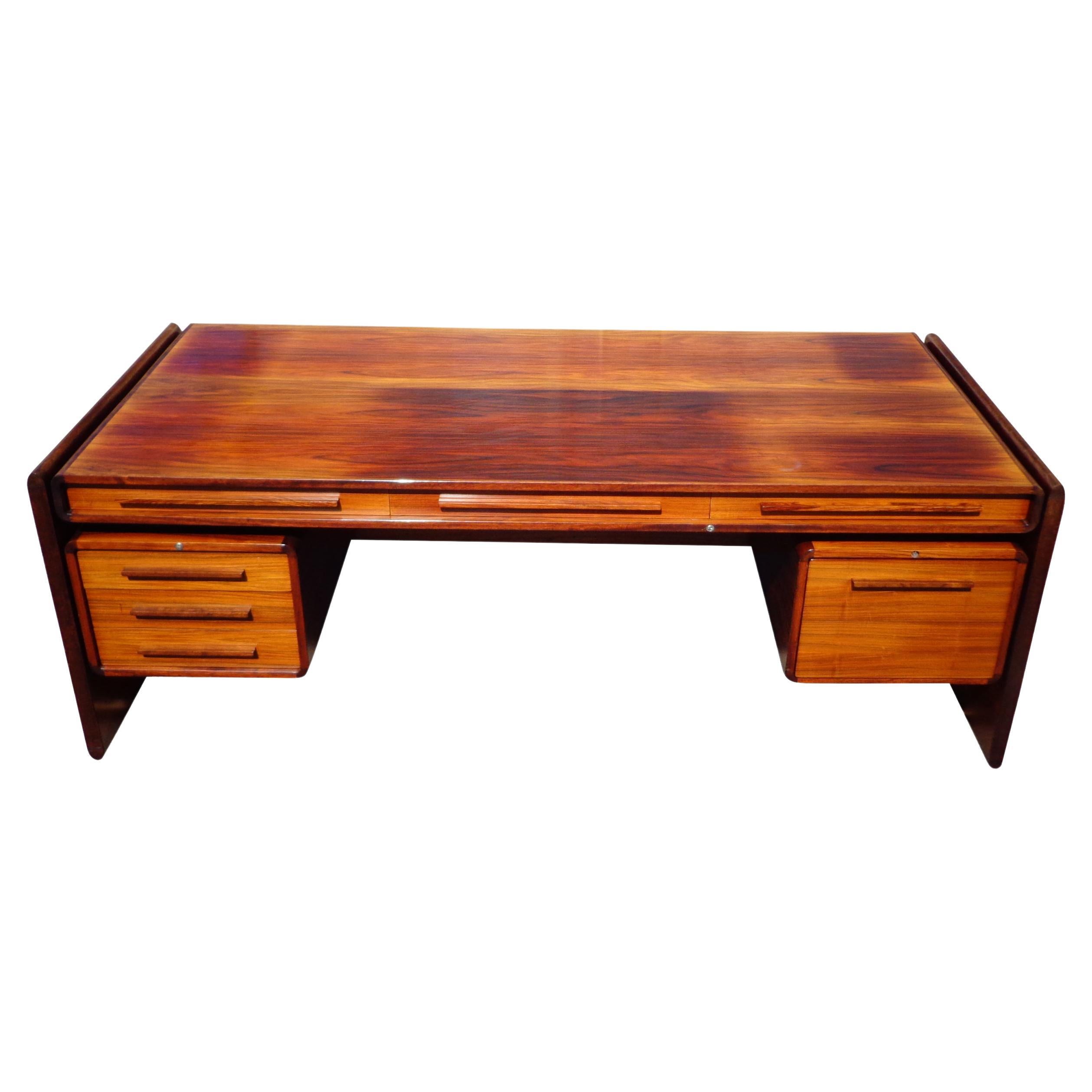 Rosewood desk from Svend Dyrlund 1970s.

A Mid-Century Modern Santos rosewood desk with panel legs and horizontal wood pulls made by Dyrlund in Denmark. Seven drawers including file storage. 
Finished back.

 Good vintage condition with age on