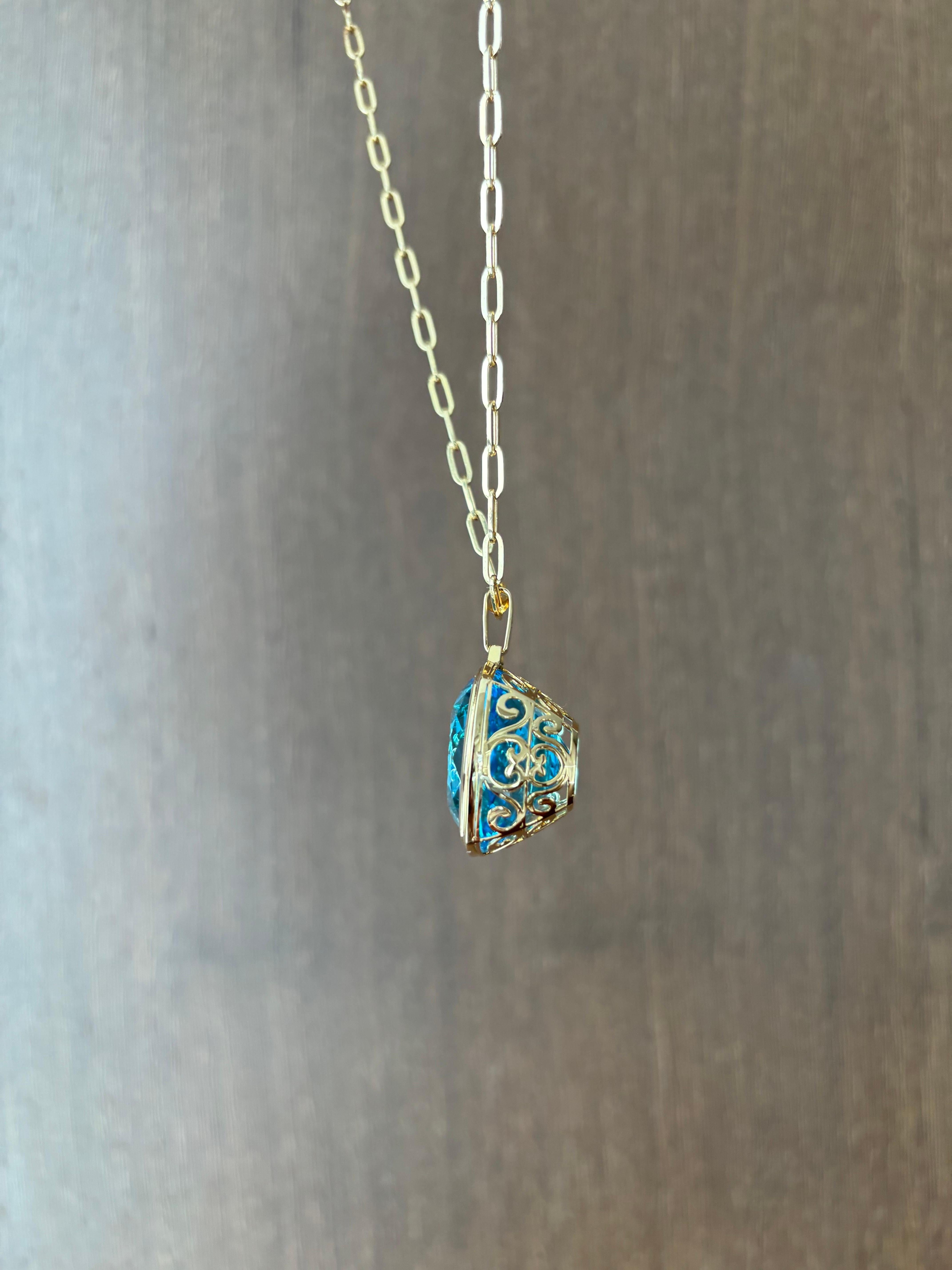A stunning, bright blue 82.46 carat cushion shaped Blue Topaz pendant, bezel set in 18K yellow gold. The natural gemstone is absolutely transparent with no inclusions, and a beautiful vivid blue color, and great luster. 
The Blue Topaz is set in