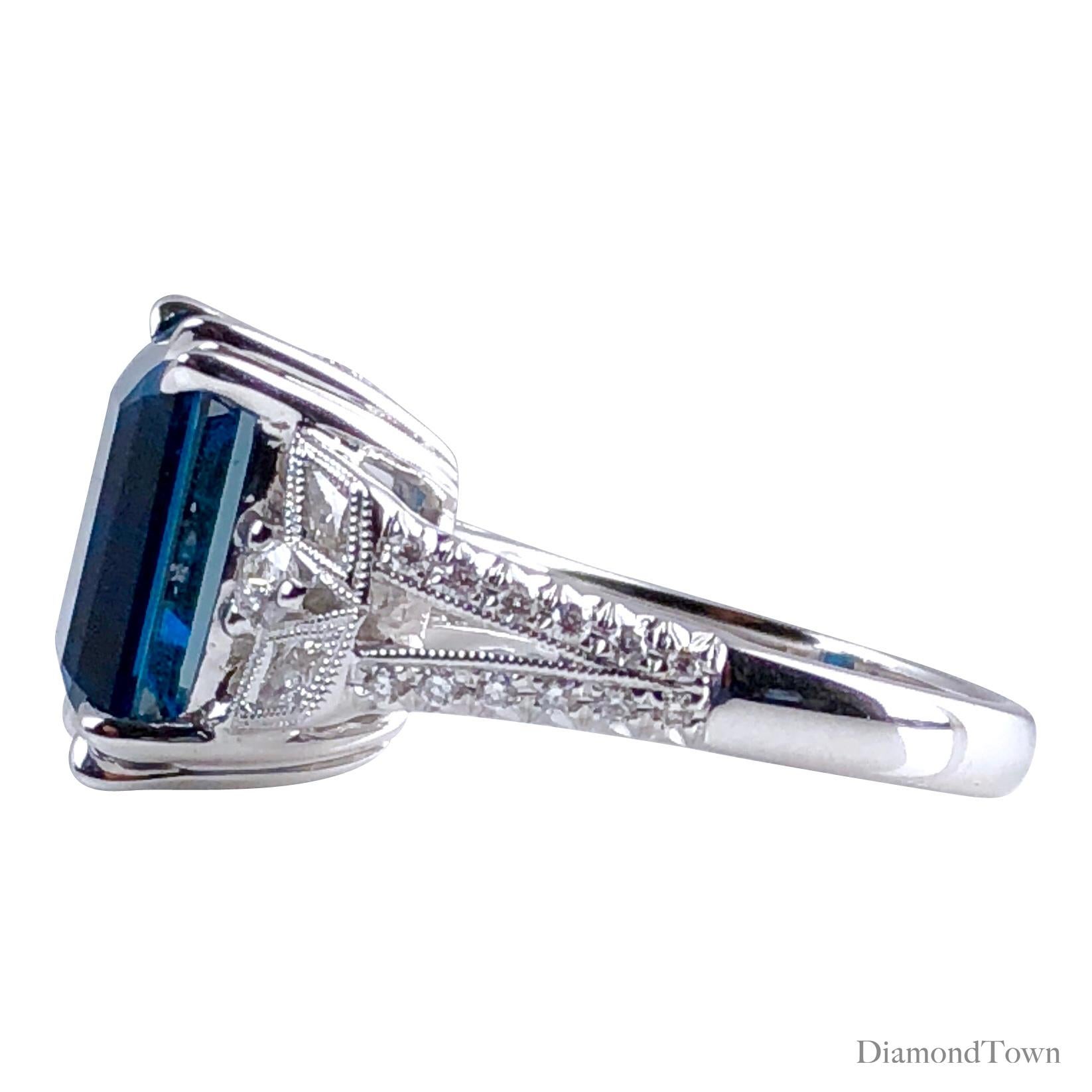 (DiamondTown) This stunning ring features a gorgeous 8.29 carat Emerald Cut Vivid Blue Topaz center, flanked by intricately detailed diamond work on all sides (total diamond weight 0.42 ct). Hand engraved milgrain work and additional diamonds down