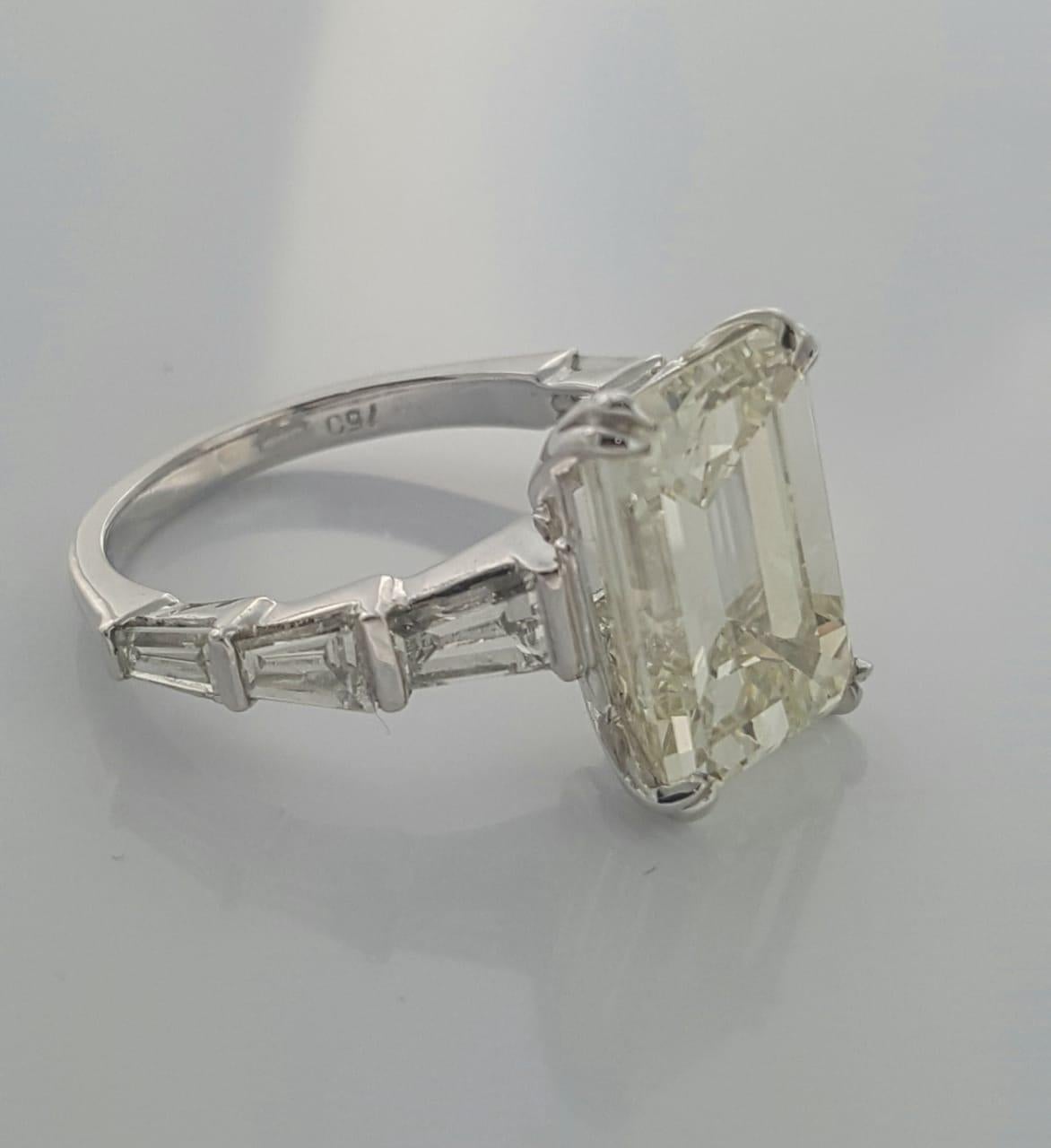 A truly gorgeous engagement ring designed and handcrafted in 18k gold  by Moguldiam Inc features 7.01 carat Emerald cut diamond with M color and SI 1 clarity and  is flanked by 6 white baguette diamonds , 3 on each side with VS clarity weighing a