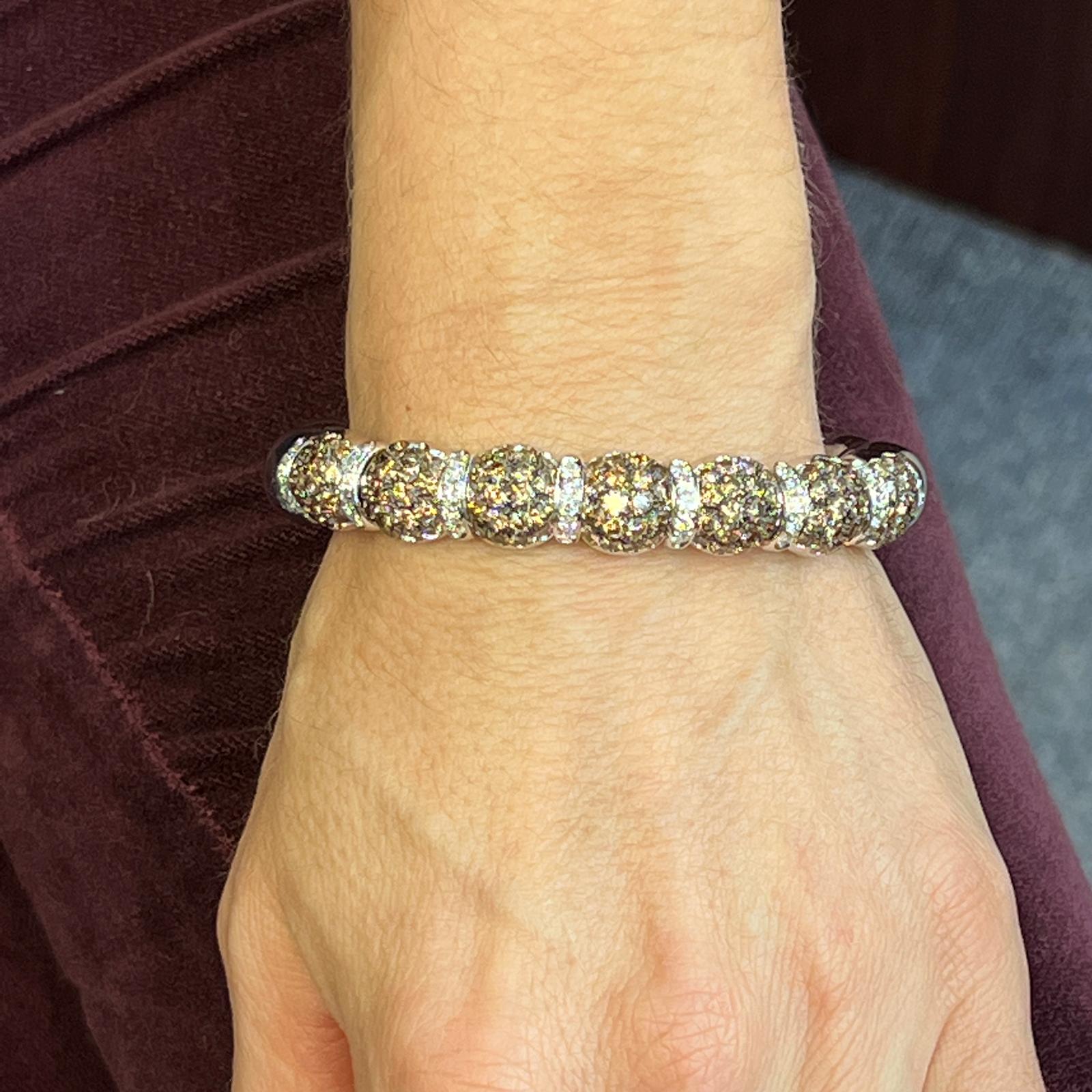 Gorgeous diamond bangle bracelet fashioned in 18 karat white gold. The flexible bangle features round brilliant white and champagne diamonds weighing approximately 8.33 carat total weight. The white diamonds are graded G-H color and VS clarity, and
