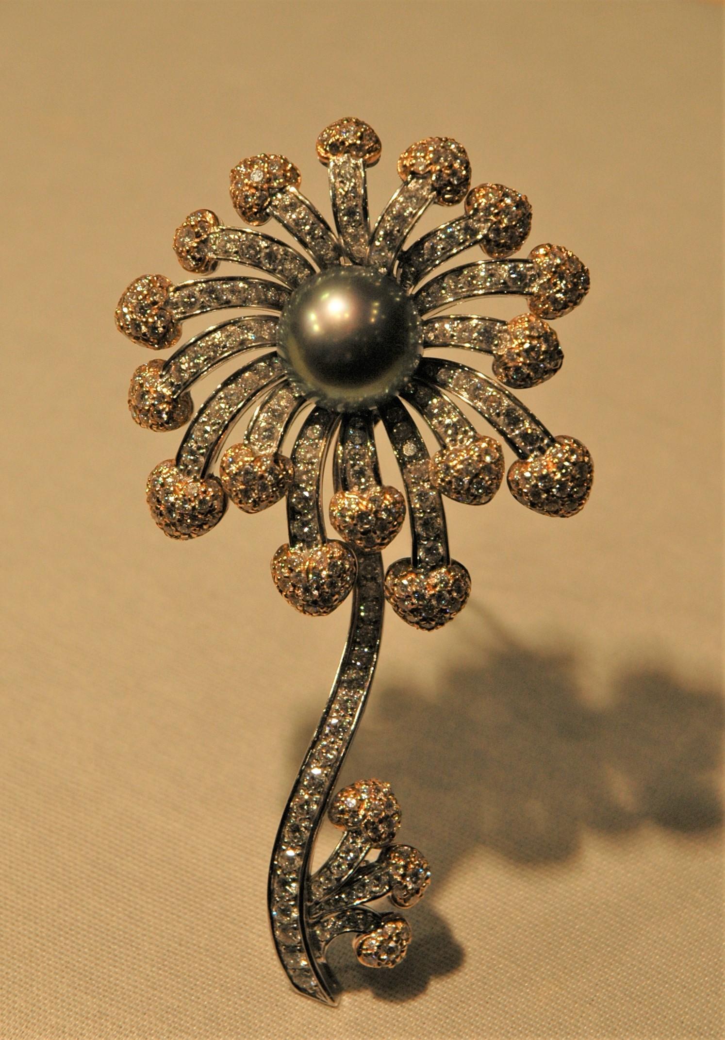 This is a wonderful flower brooch, made in white gold with diamonds (8.36 carats) set all over the jewel. It is formed by a big corolla with a perfect tahity pearl in the center, the petals ending with yellow gold hearts, always covered by a