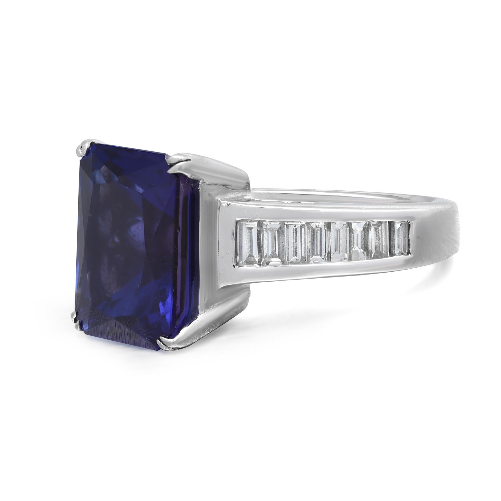 This luxurious engagement ring features prong set emerald cut violetish blue Tanzanite as the center stone with channel set baguette cut diamonds set halfway through the band. Crafted in 18K white gold. Total Tanzanite weight: 8.47 carats. Total