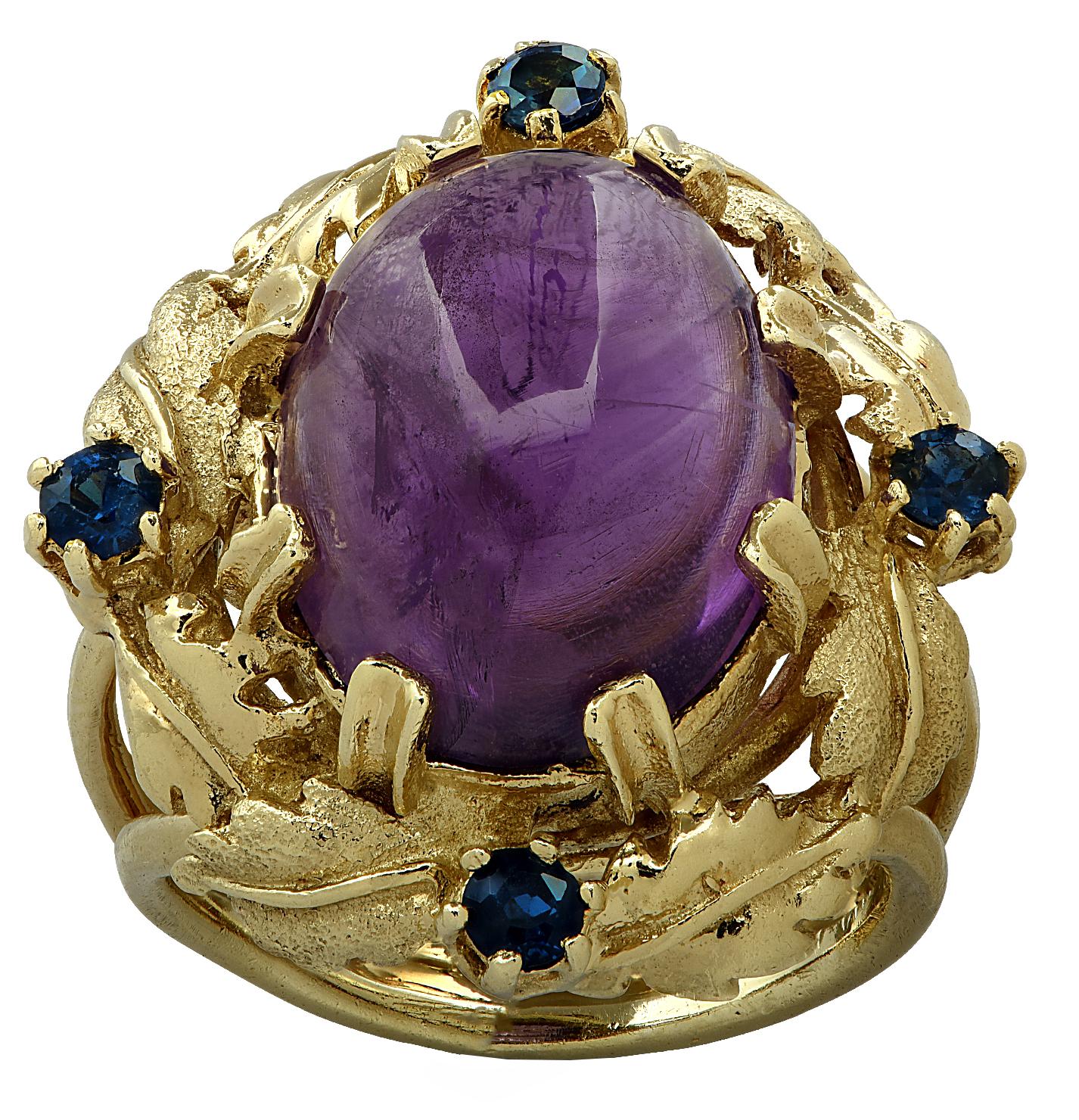 Stunning cocktail ring crafted in 18 karat yellow gold showcasing a spectacular oval Amethyst cabochon weighing approximately 8.5 carats, resting on a bed of gold leaves, adorned with 4 round sapphires weighing approximately .25 carats total.  The