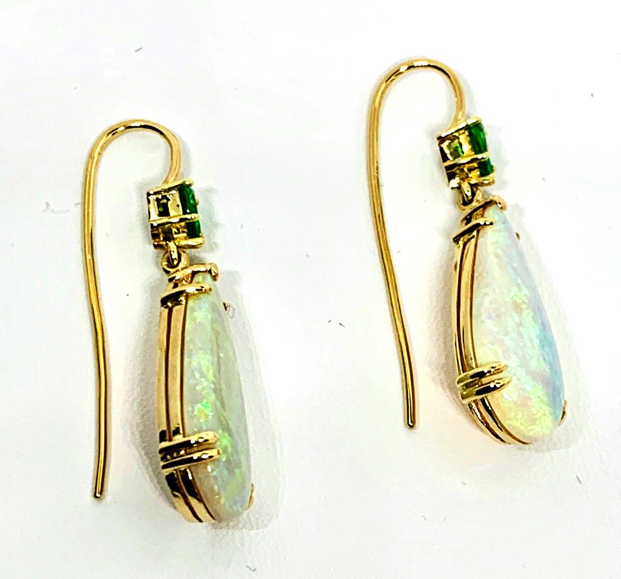 These stylish drop earrings feature beautifully kaleidoscopic opals and bright green tsavorite garnets set in 18k yellow gold. The large, colorful pear-shaped gems are beautifully matched and pair perfectly with the sparkling  African green garnets.