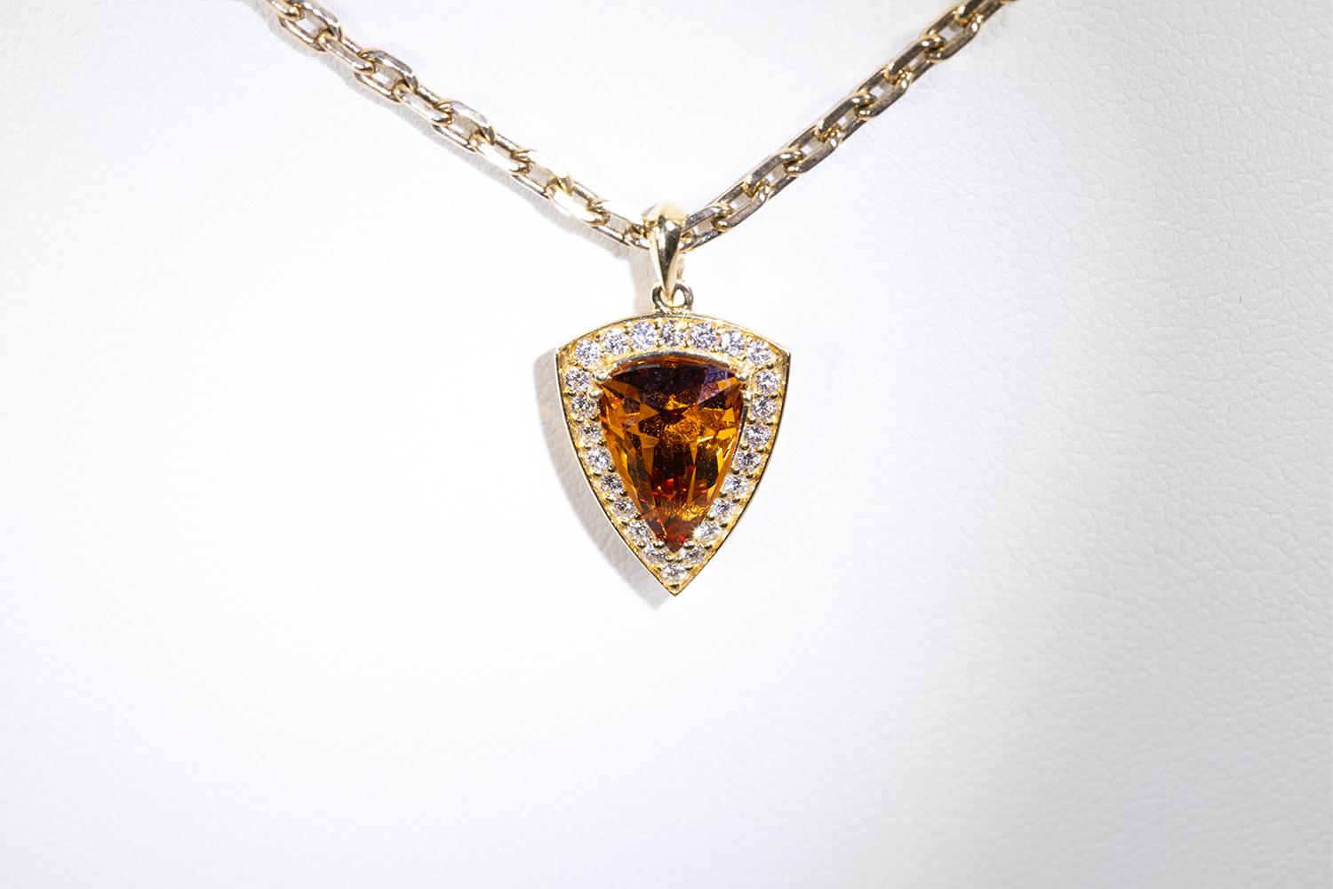This is a beautiful richly colored 3.52 Carat Hessonite Garnet pendant of excellent quality. The trillion shaped stone is set in a Halo Pendant of 24 Diamonds that have a total weight of 0.312 Carats. The pendant is on a classic gold chain that