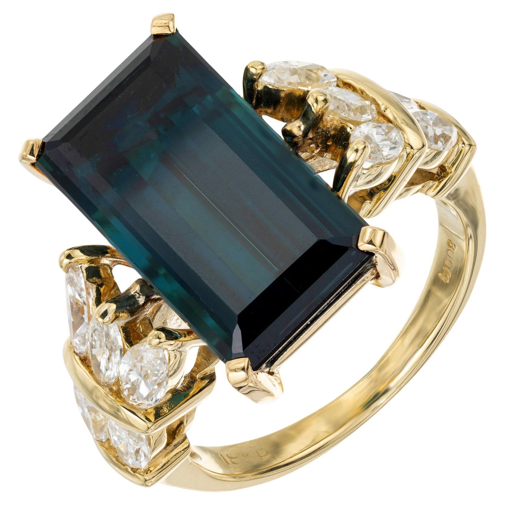 1960's Blue green Indicolite Tourmaline and diamond ring. This timeless piece starts with an Emerald cut greenish blue Indicolite Tourmaline center stone, totaling 8.55cts. The mounting is 18k yellow gold and adorned with five Marquise accent