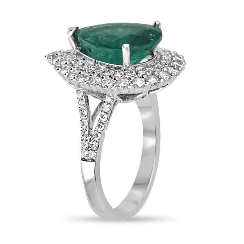 This stunning engagement ring showcases an impressive 7.53-carat pear-cut emerald sourced from the renowned mines of Zambia, exuding a rich dark green hue with captivating semi-transparent clarity. Two radiant diamond halos encircle the emerald,