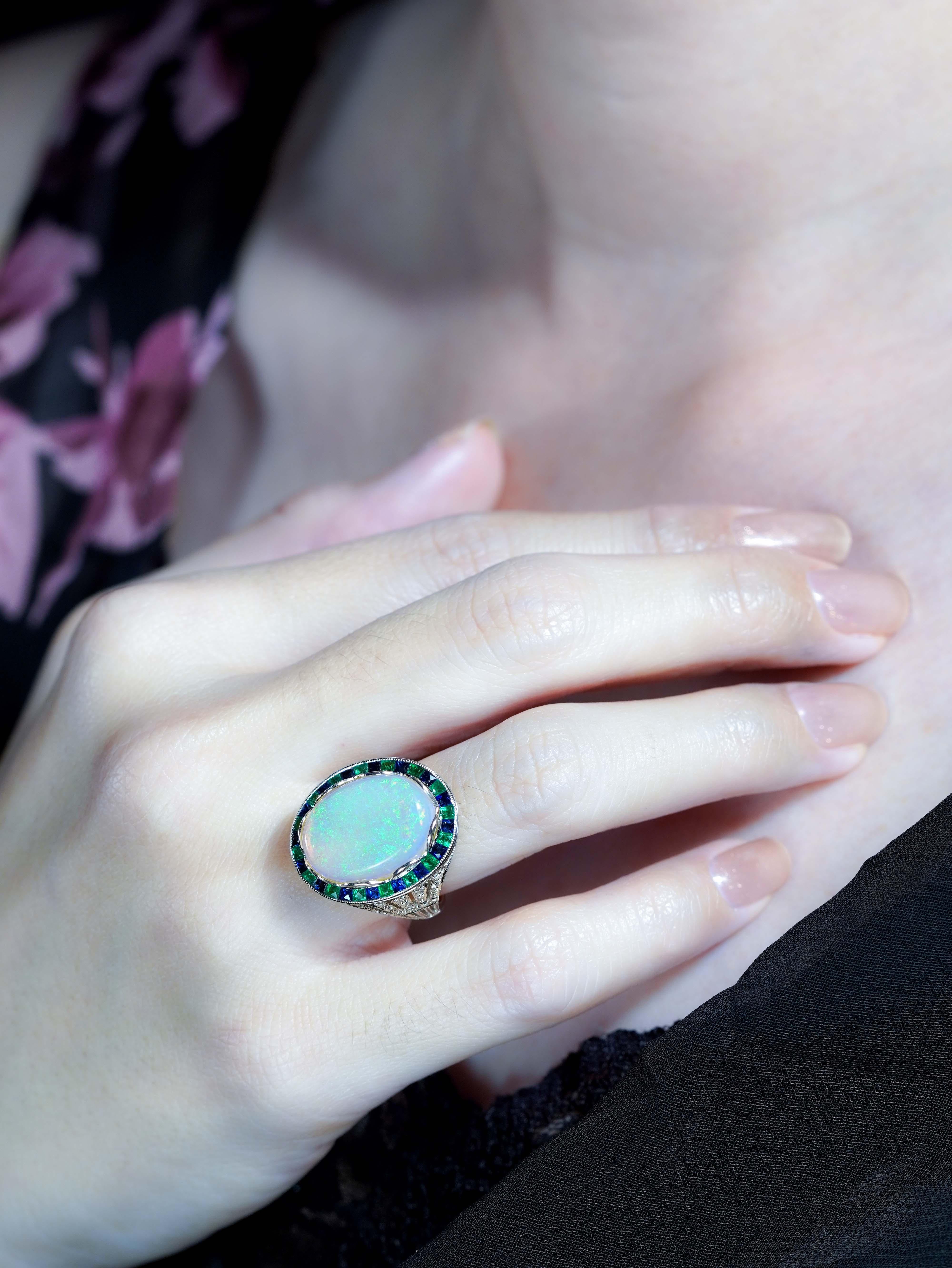 Radiating vintage charm, this Art Deco style cocktail ring features a luminous opal at the center.Encircled by vivid French-cut emeralds, the design glows with color and elegance.Diamond-accented shoulders add sparkle and sophistication to every