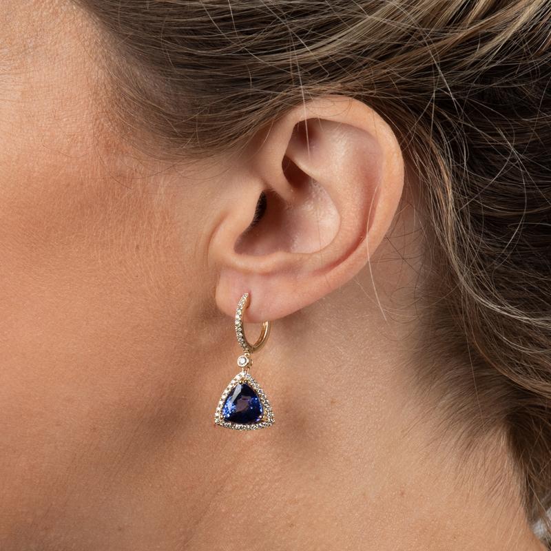 These dangle earrings feature two trillion cut natural tanzanites weighing 8.76 carats accented by 0.78 carat total weight in round brilliant cut diamonds set in 14 karat yellow gold. They are set on a huggie hoop earring. 
Measurements: Length