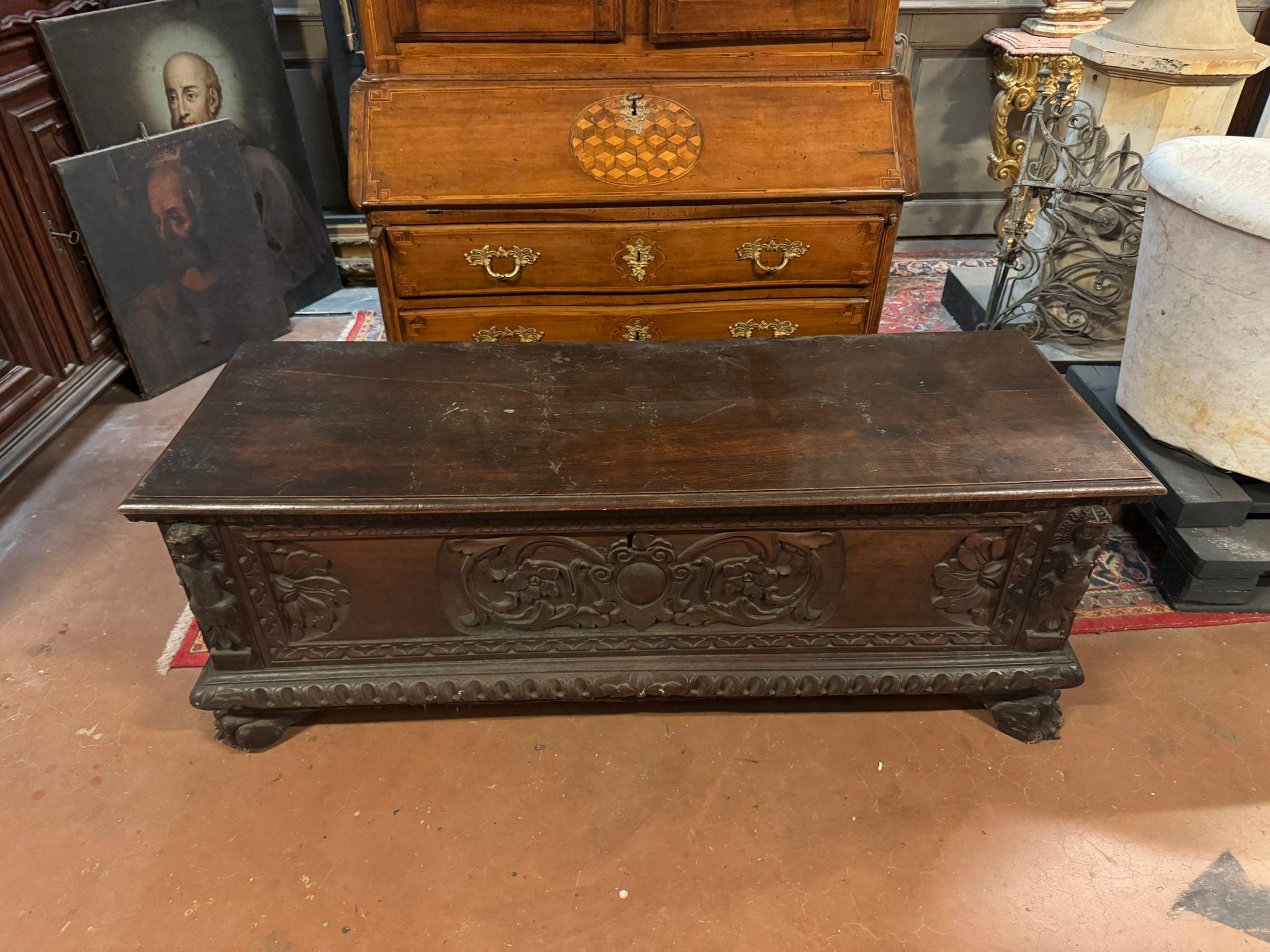 An elegant and imposing antique carved chest, crafted from solid dark walnut, finely handcrafted.
The front panel is richly carved with plant and floral decorations, scroll motifs, and a cartouche or oval shield in the center, likely intended for a