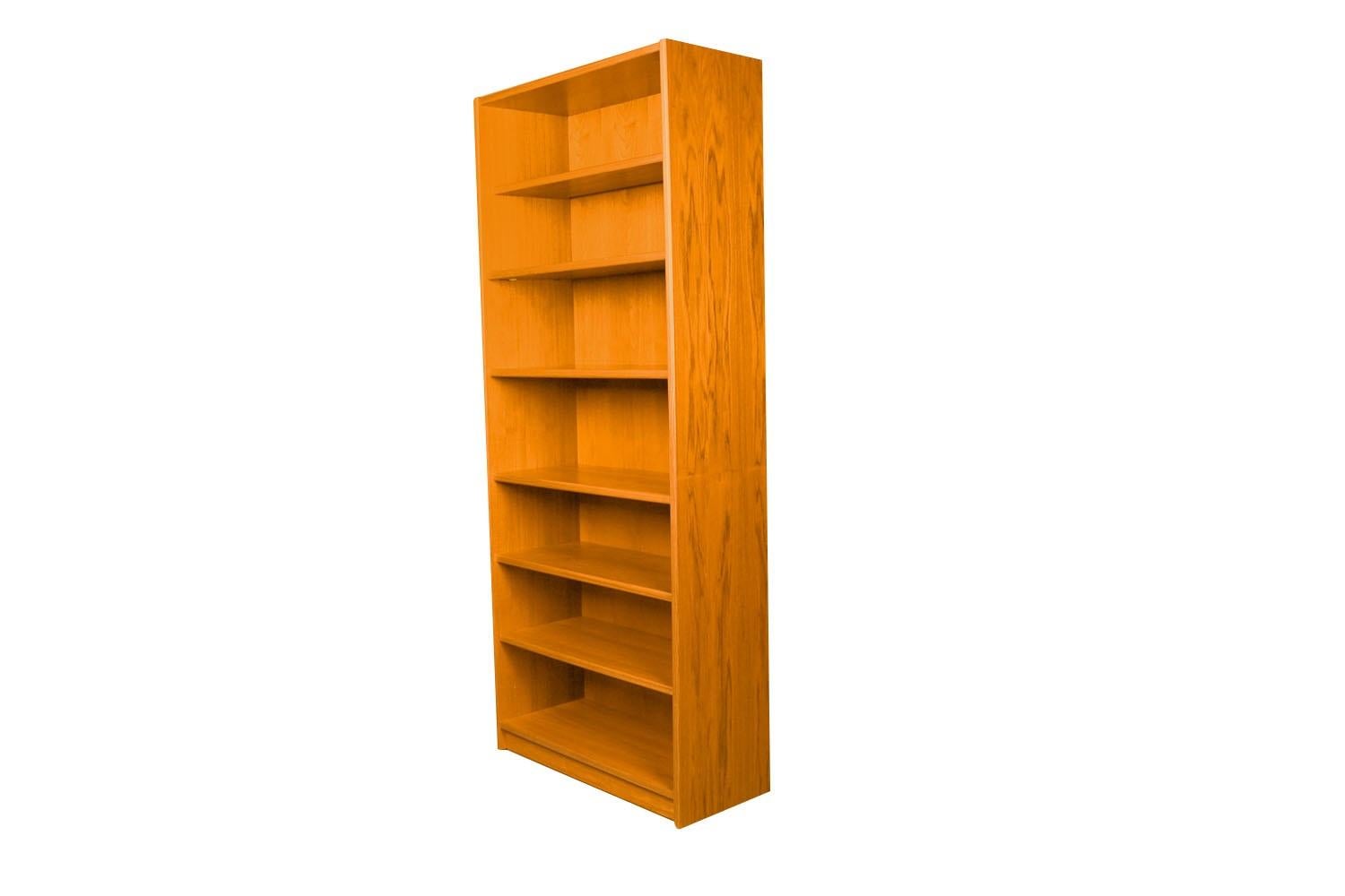 An exceptional teak tall bookcase made in Denmark.  Gorgeous Mid-Century Modern Teak bookcase / tall bookshelf unit. Beautiful, minimalist, clean, straight lines. Features five and one stationary providing ample storage space. The top shelf is 11