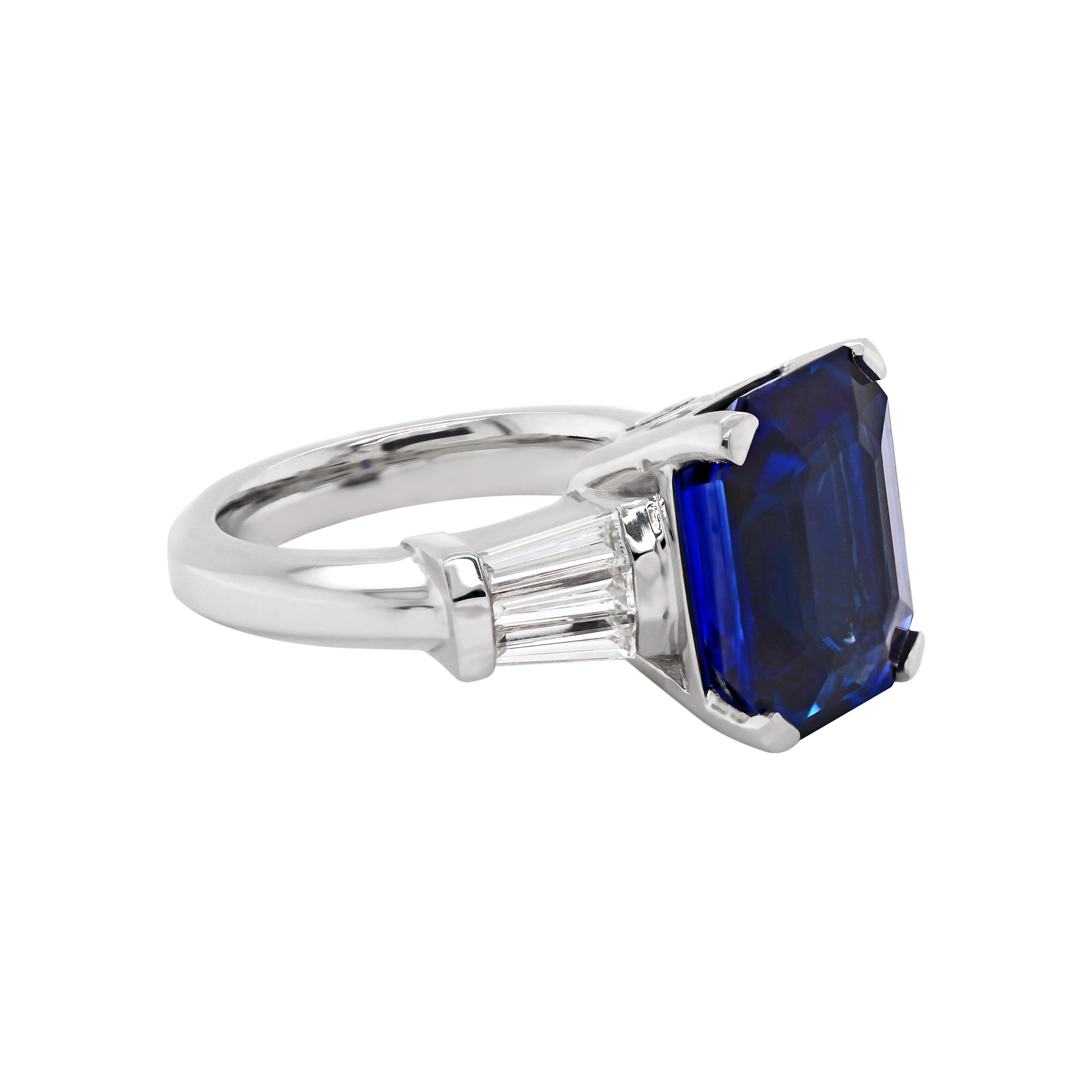 Exquisite engagement ring set with an emerald cut royal blue sapphire weighing an impressive 8.88 carats in a four claw open back setting. The sapphire is accompanied by three tapered baguette cut diamonds on each shoulder with a combined weight of