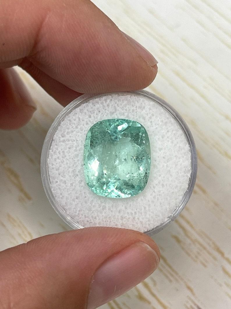 Stone: Emerald
Weight: 8.94-carats
Shape: Cushion Cut
Clarity: Transparent
Luster: Very Good
Color: Light Green
Measurements: 14.76mm x 12.63mm x 7.75mm
Geographic Origin: Colombia
Treatment: Natural, Oiling

Comments: Due to their growth conditions