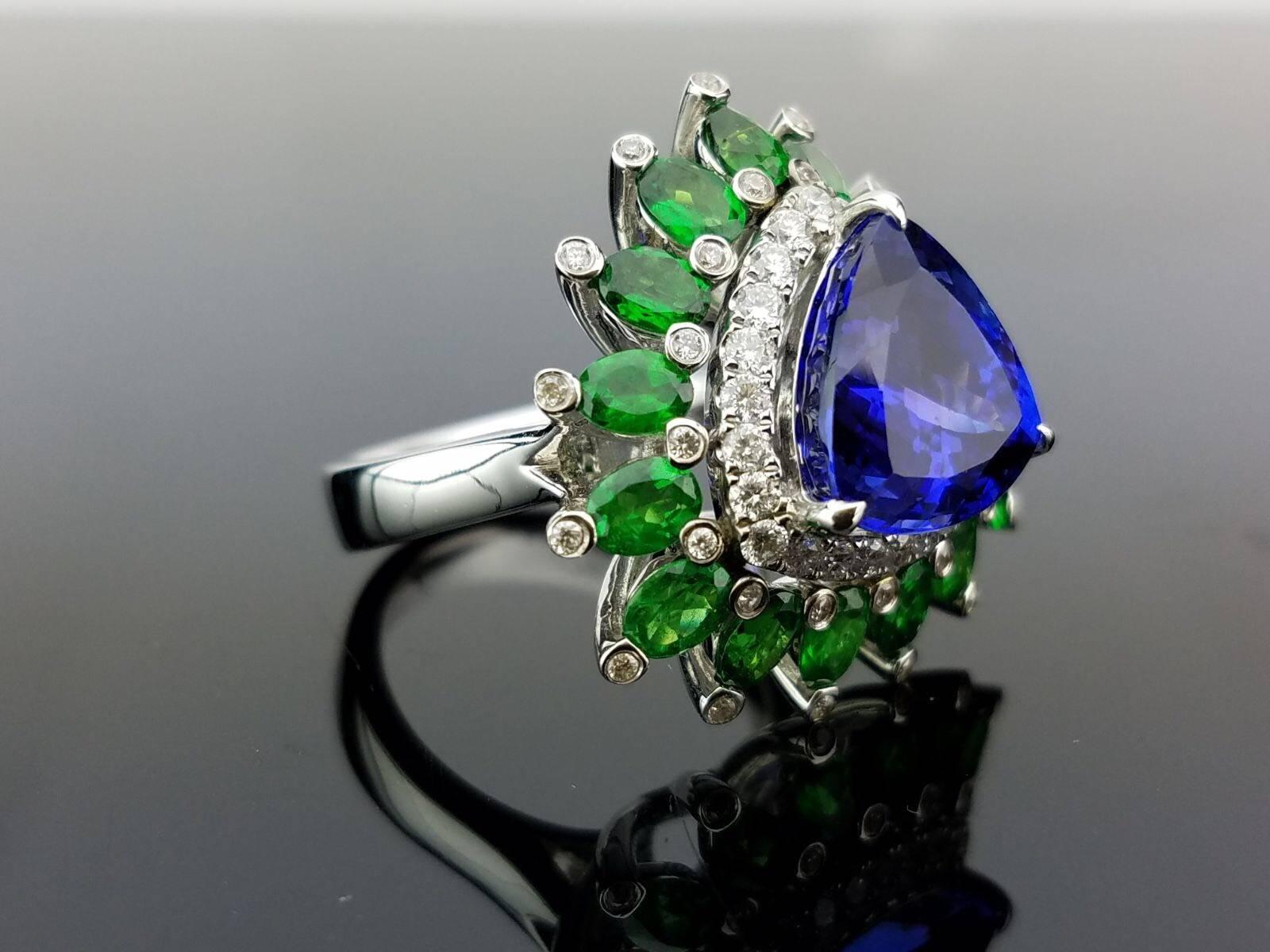 A unique trillion shaped, eye clean Tanzanite and Green Garnet cocktail ring with diamonds, all set in 18K white gold. 

Stone Details: 
Stone: Tanzanite
Carat Weight: 8.96 Carats

Diamond Weight: 0.62 Carats

Currently a ring size US 6, but we can