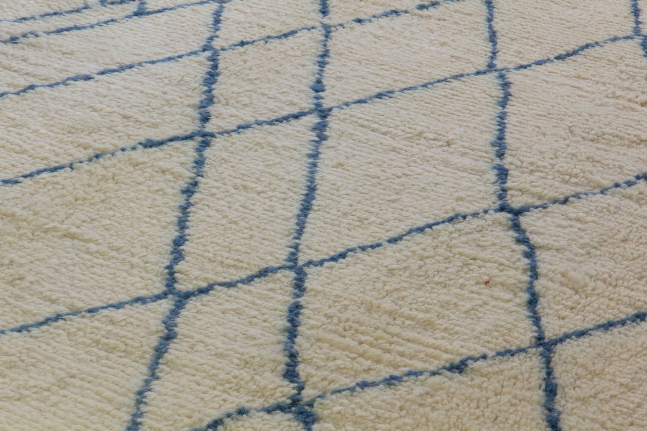 Tapis moderne fait main en laine de mouton, de couleur bleue et ivoire naturel non teinté, présentant un motif de treillis irréguliers en forme de losanges. Le tapis a un poil de laine doux et lustré.
Il est disponible tel quel. Nous pouvons