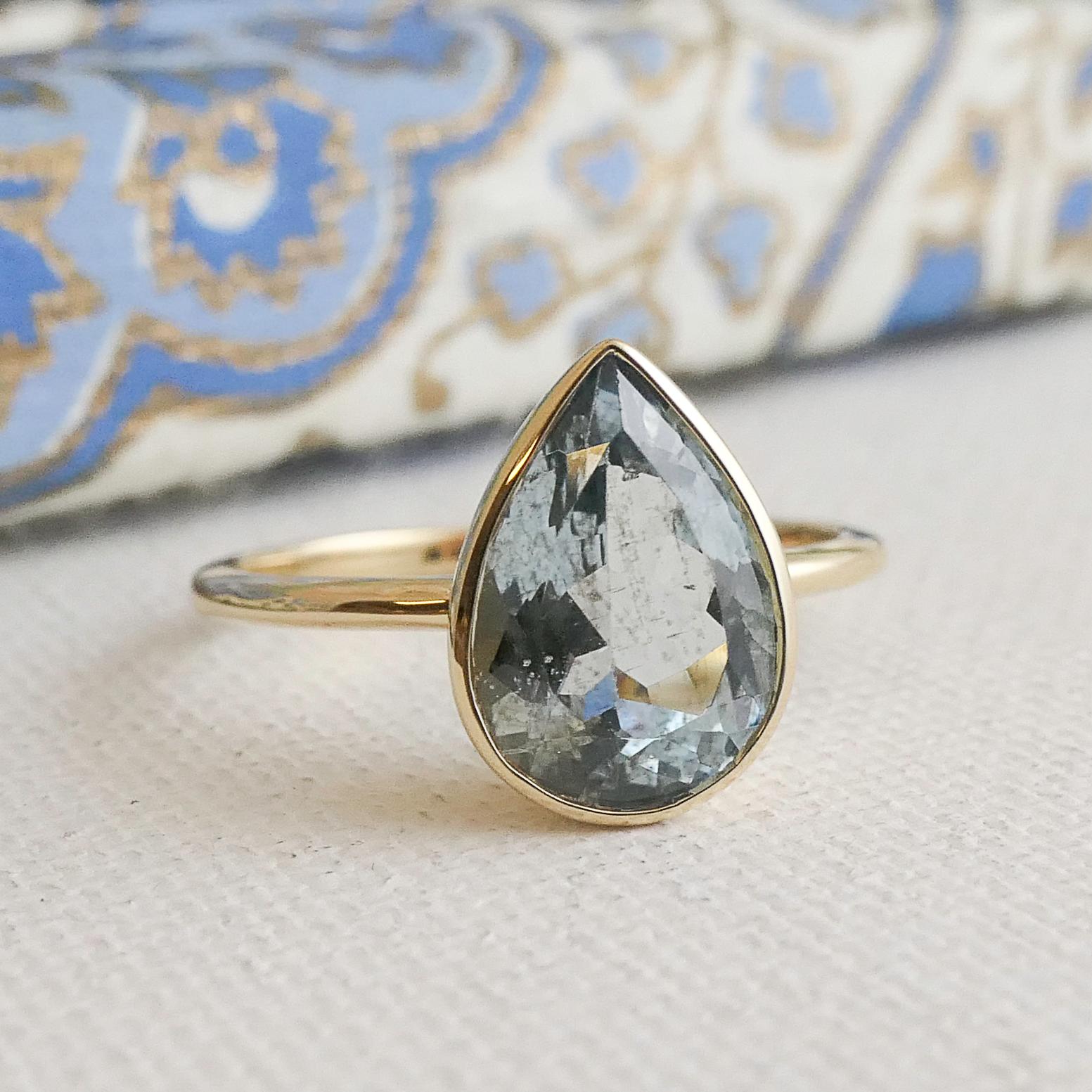 Cette élégante bague est ornée d'une aigue-marine de 8 x 11 mm sertie dans un élégant chaton en or jaune 14 carats. La teinte bleue pâle et douce de l'aigue-marine contraste magnifiquement avec les tons chauds et dorés, créant un look intemporel et