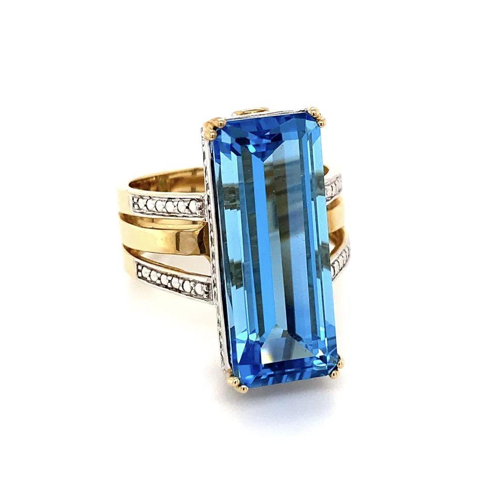 Simply Beautiful! Finely detailed Solitaire Blue Topaz with Diamond Surround Gold Cocktail Ring. Centering a securely nestled Hand set 9 Carat Blue Topaz Emerald-Cut Gemstone. Enhancing the shank on either side, Round Brilliant Cut Diamonds,