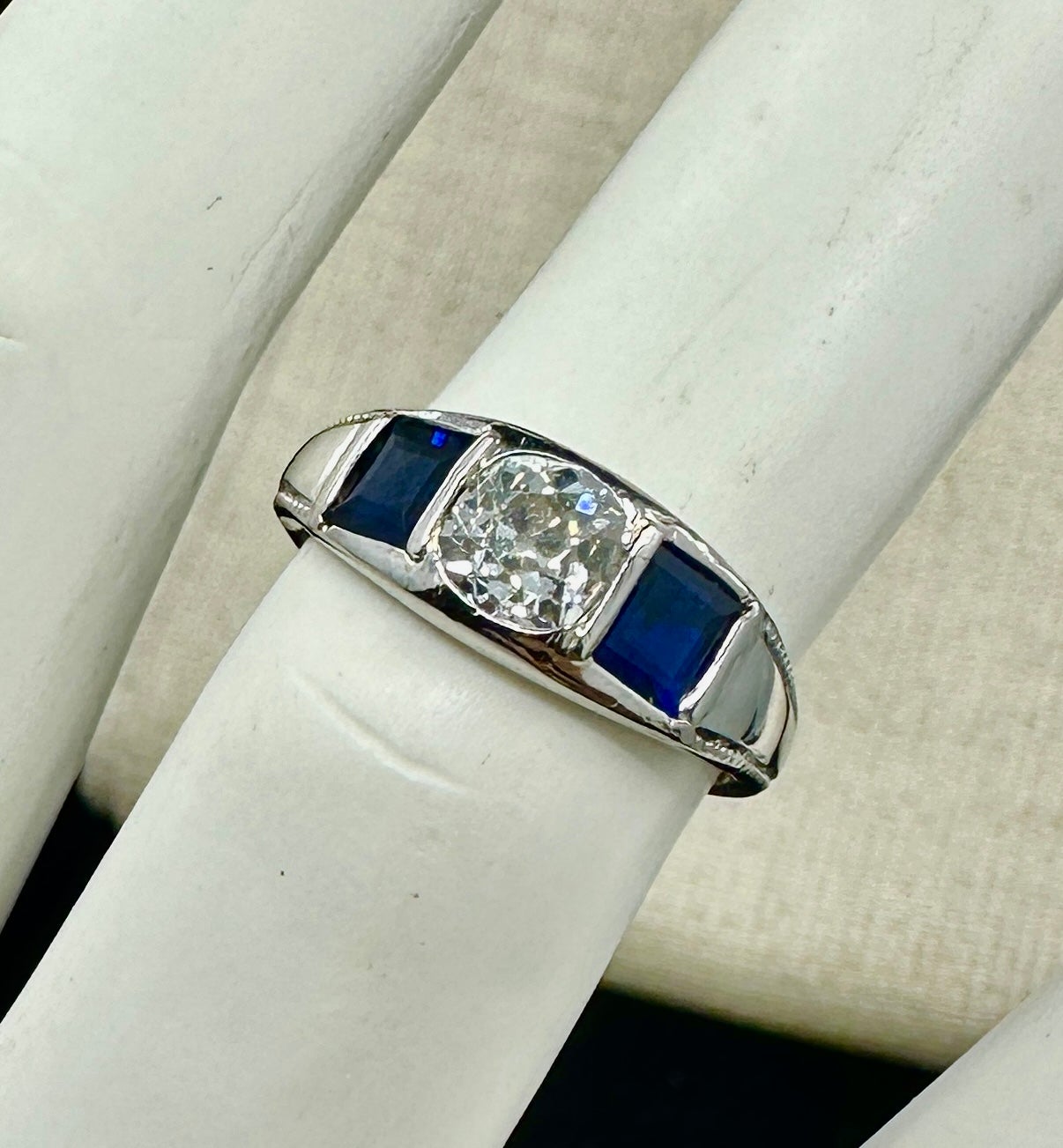 Este es un impresionante anillo de compromiso de boda Art Decó antiguo de tres piedras de 0,9 quilates de diamante natural talla antigua y zafiro talla princesa en platino.  El clásico anillo Art Déco está centrado por un diamante talla Mina Antigua