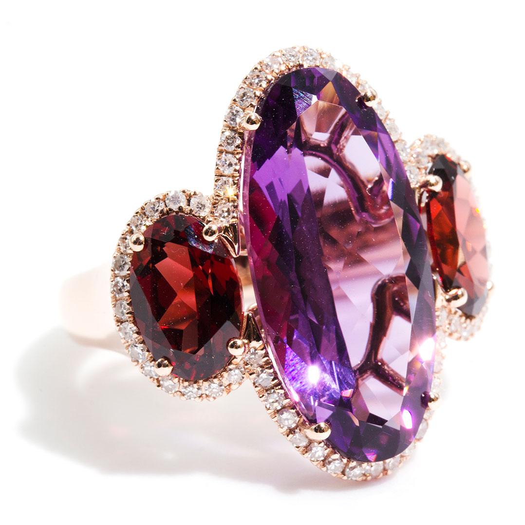 Crafted in 9 carat rose gold is this uniquely vintage ring boasting a glorious 8.8 carat vivid deep purple Amethyst. It is accompanied by two oval deep red Garnets. This trilogy is beset with sparkling round brilliant cut diamonds. We have named