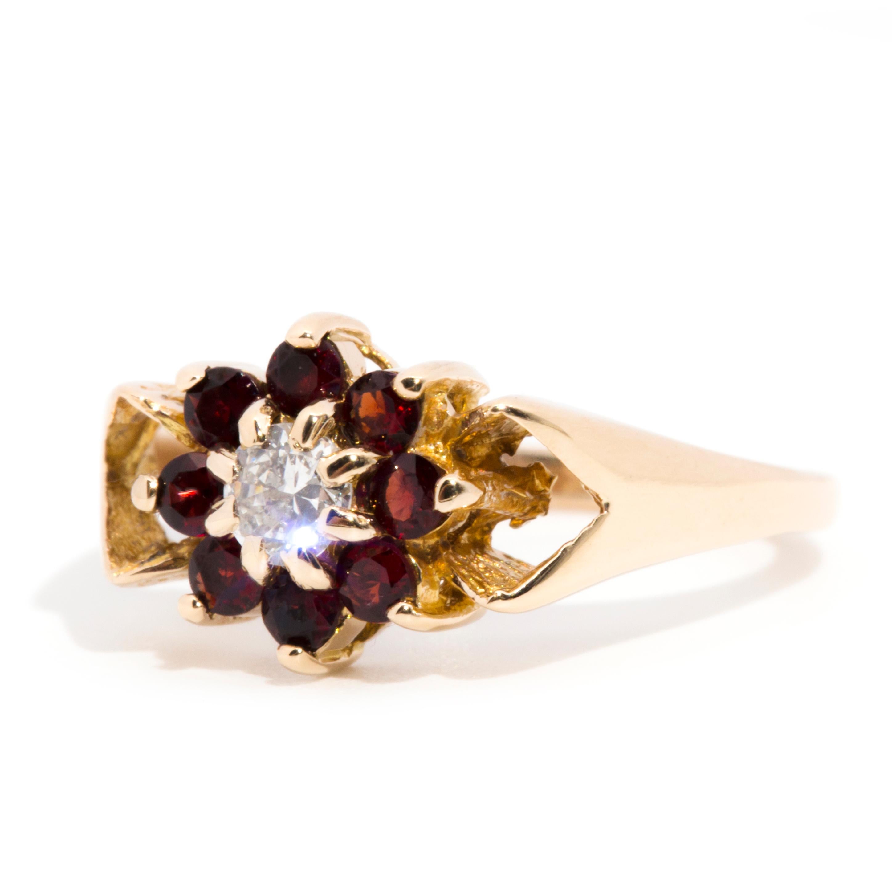 Crafted in 9 carat yellow gold, this darling vintage cluster ring, circa 1980s, is ever so charming with her shimmering flower-shaped cluster embellished with a glistening round brilliant cut diamond surrounded by a halo of gorgeous garnets. This