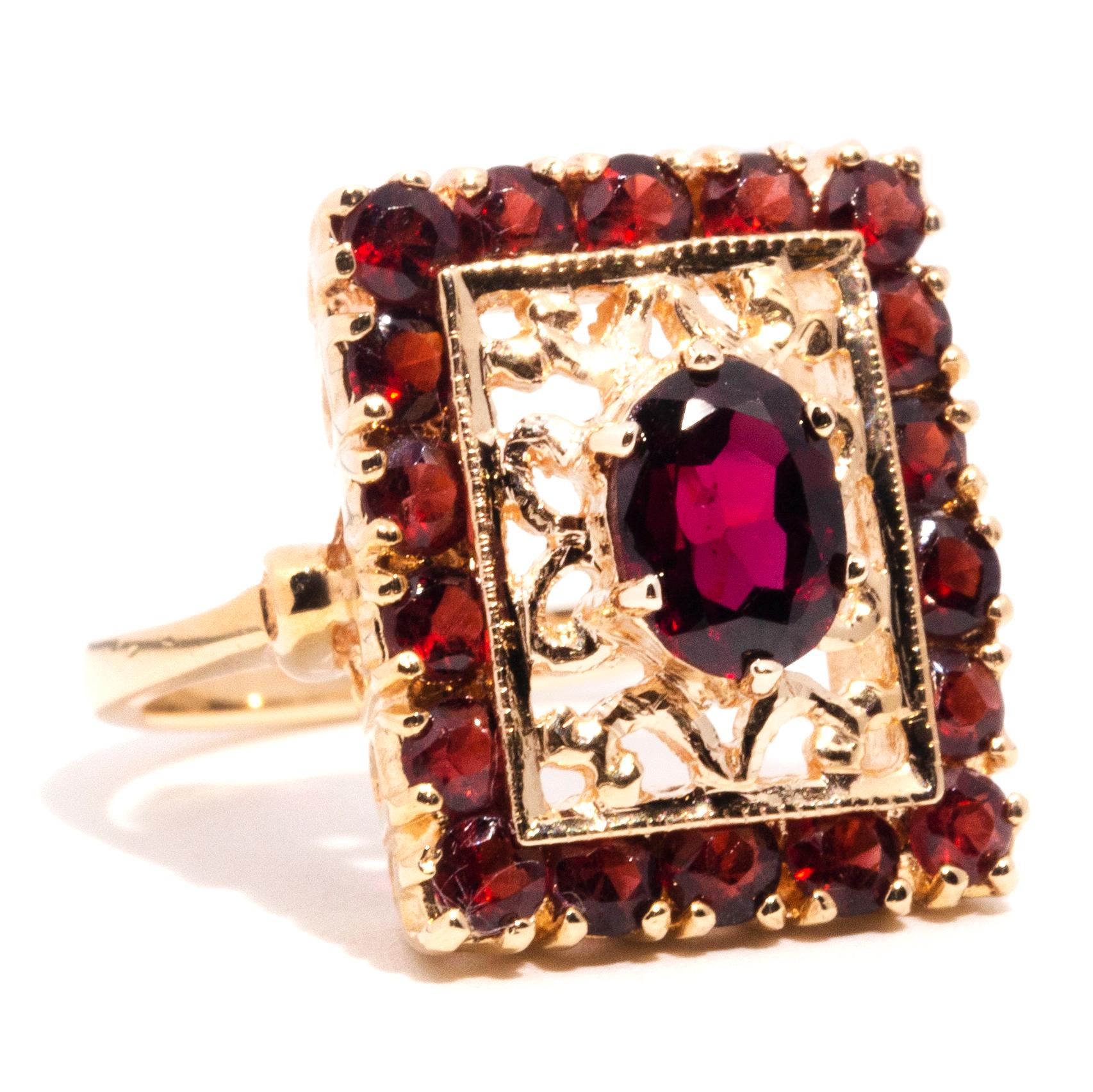 Crafted with 9ct yellow gold, this ornate vintage halo ring features a gorgeous filigree gallery home to an alluring oval faceted garnet encompassed by a rectangular halo border of smaller shimmering garnets. We have named this vintage splendour The