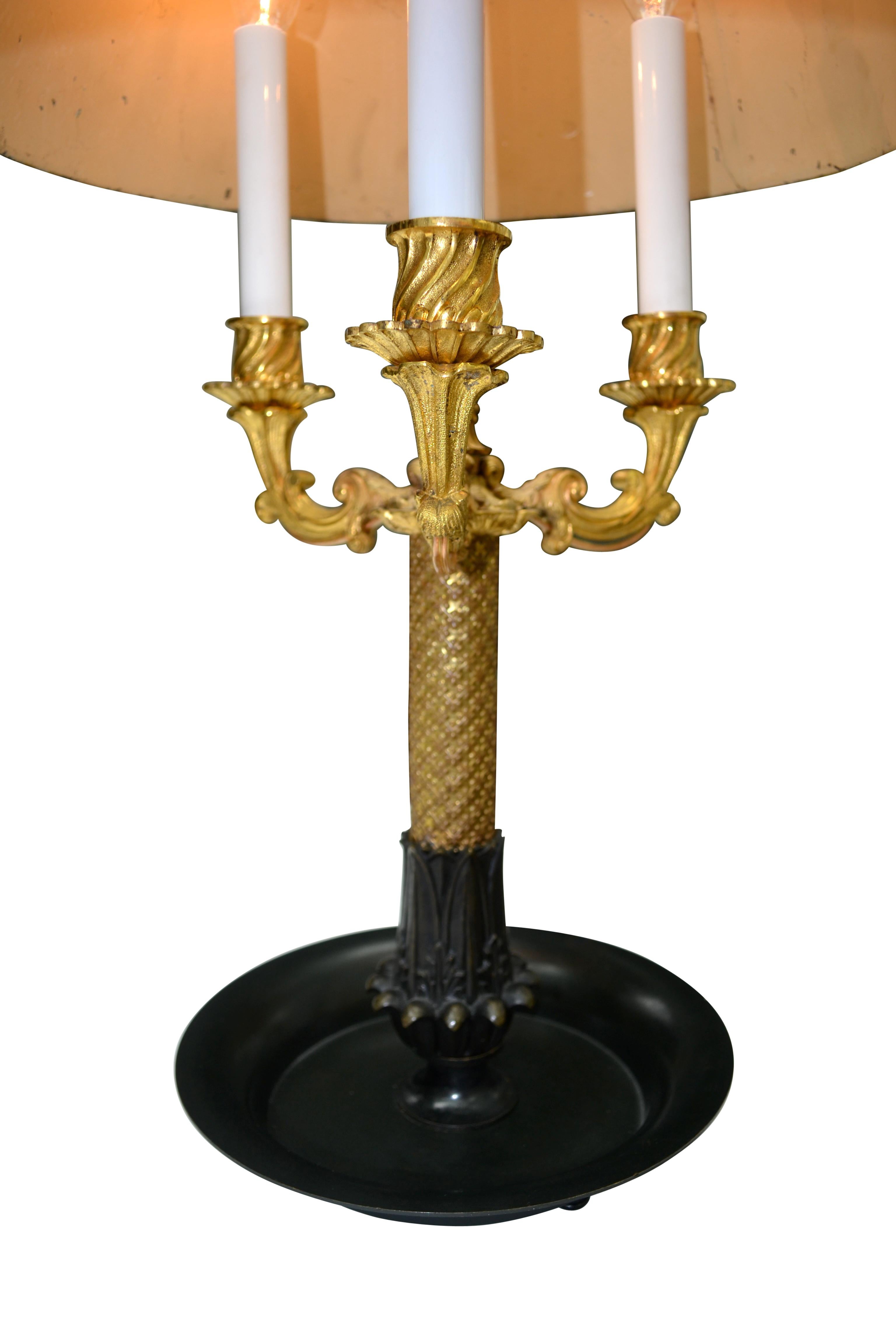 A patinated and gilded bronze Bouillotte lamp in well chased and gilded bronze having three candle arms. Presented with an adjustable painted anthemion decorated tole metal shade.