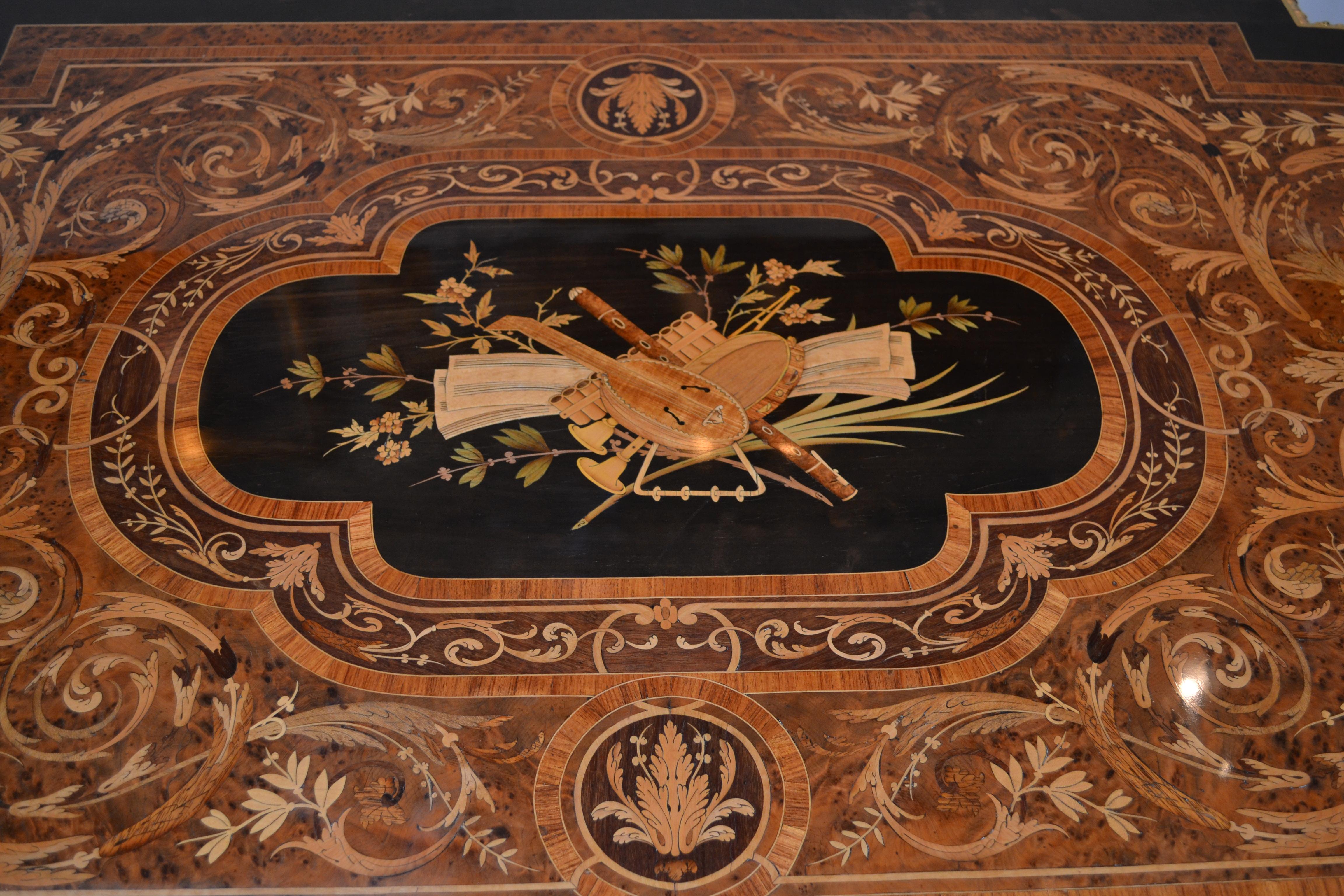 A French Napoleon III D ended table exedra shaped top richly inlaid with various wood species including burl wood kingwood satinwood and ebony centered with a large classic urn, birds nest and flowers. The entire top is edged with ormolu banding and