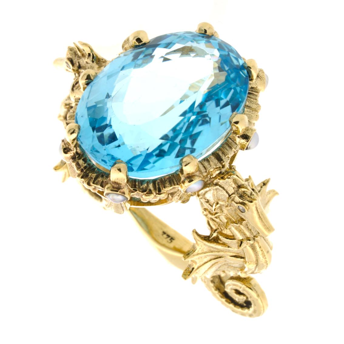 Hand crafted in 9kt yellow gold, the Crowned Oceanides Ring is a breathtaking jewel to behold. It features a luminescent 20.38ct natural oval cut Swiss blue topaz perched in all it's glory atop a garland crown studded with eight 2mm natural pearls,