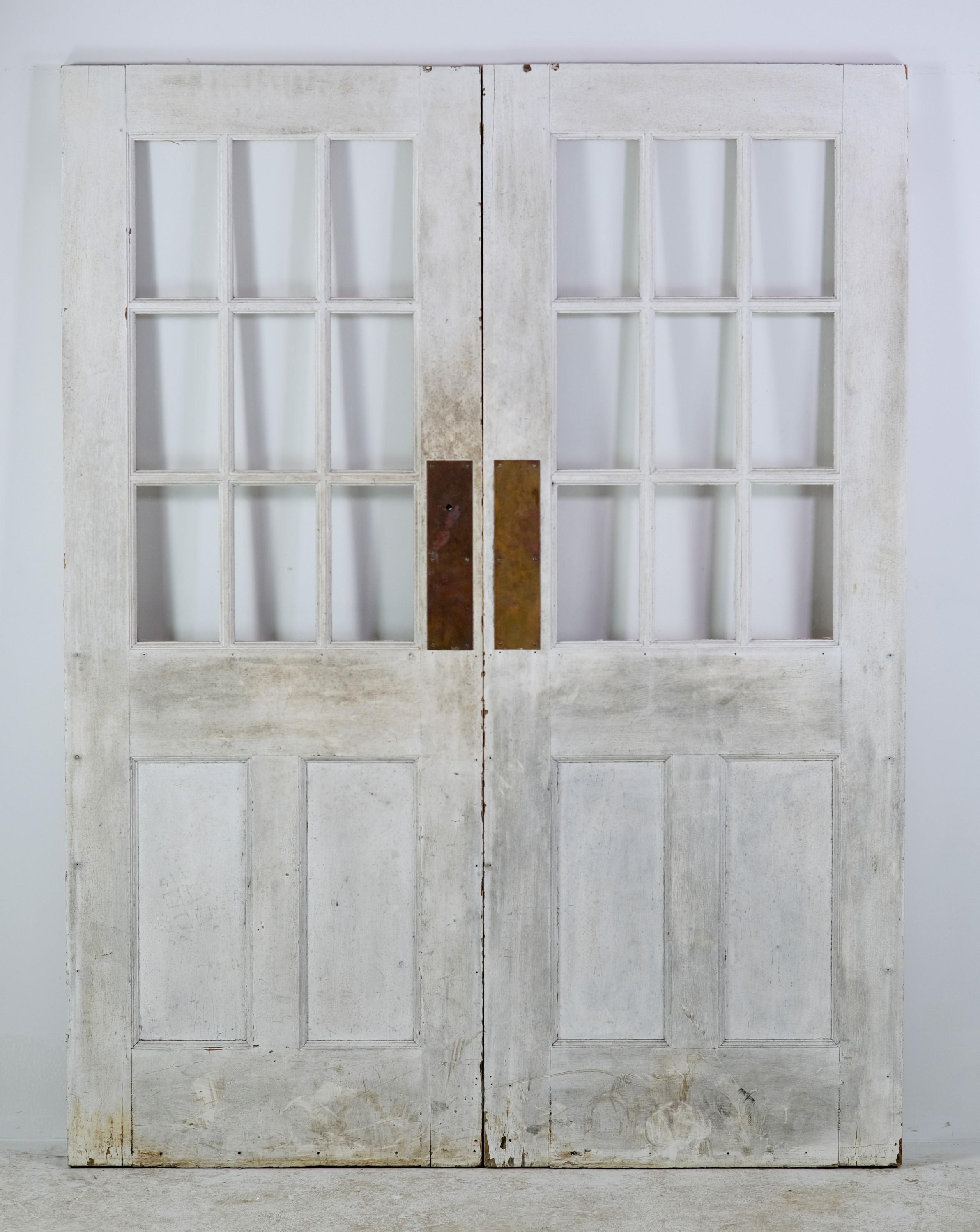 Set of antique commercial oak doors with nine glass lites and two vertical wood panes at the bottom. They come complete with original brass door pulls. One side is painted beige and the other side painted white. Priced as a double. This can be seen
