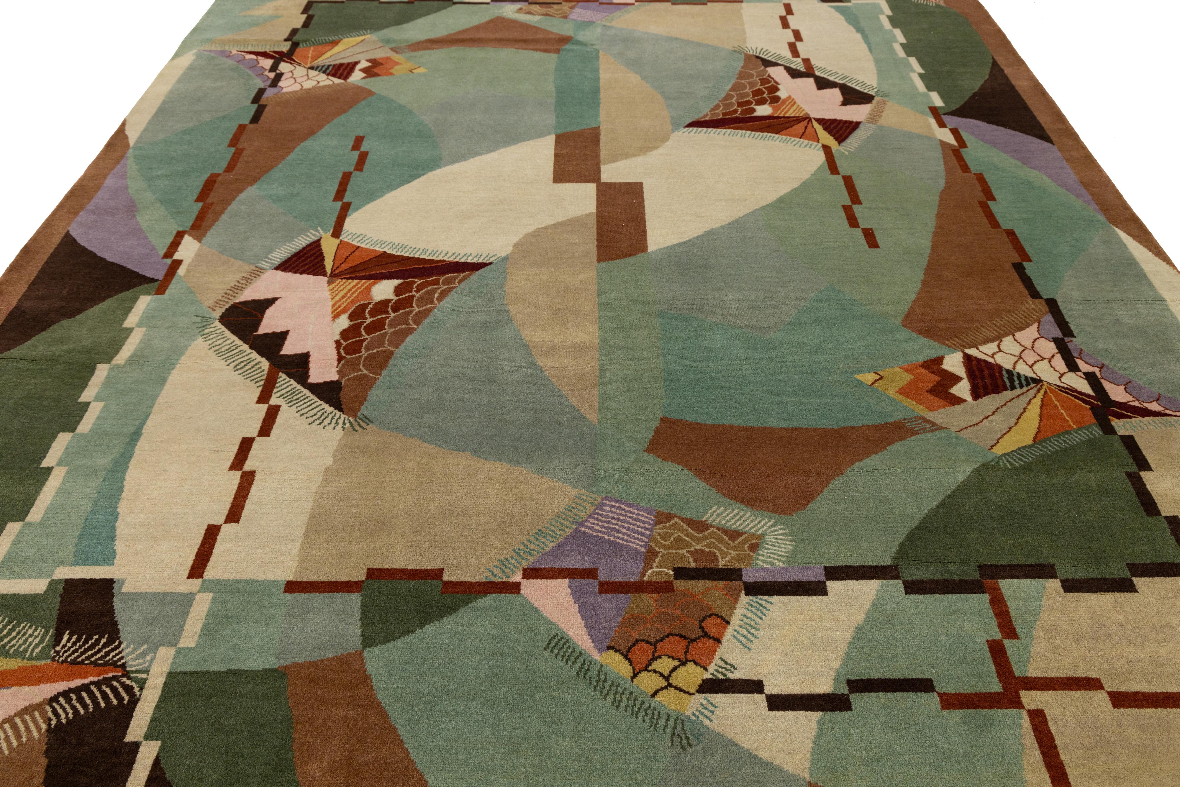 Dieser atemberaubende, handgeknüpfte Wollteppich zeigt eine wunderschöne grüne Farbpalette, die durch zarte braune und mehrfarbige Details akzentuiert wird, die das raffinierte Allover-Design im Art-Deco-Stil perfekt unterstreichen.

Dieser Teppich