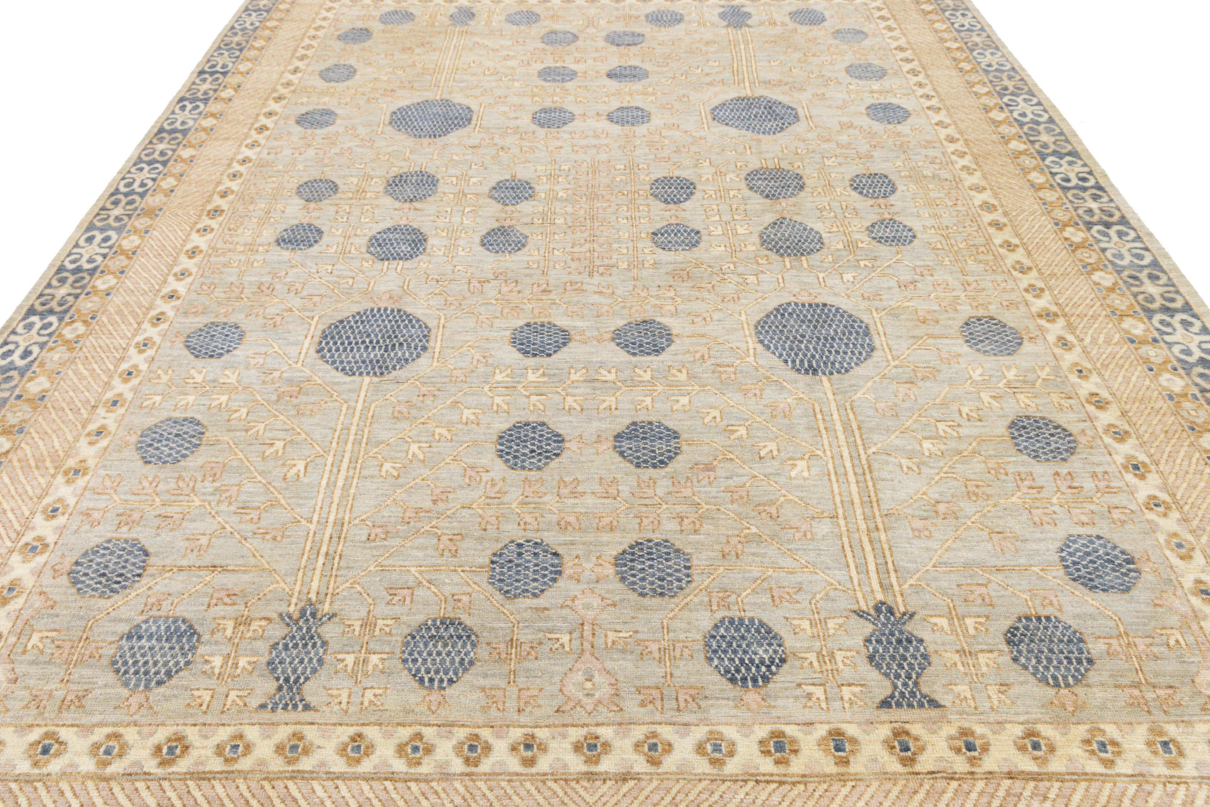 Dieser handgeknüpfte Wollteppich im Khotan-Stil hat einen weichen nebelgrauen Hintergrund, der durch zarte Akzente in Gold, Rosa, Beige und Blau wunderschön akzentuiert wird. Das verschlungene All-Over-Interlock-Muster verbindet gekonnt