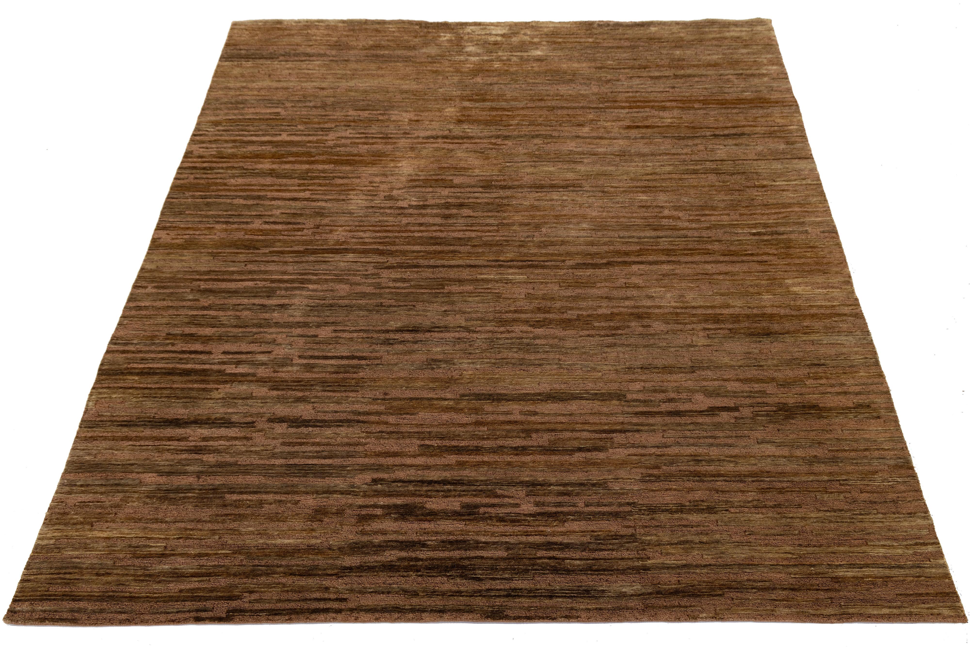 Dieser moderne, in Indien handgewebte Wollteppich zeichnet sich durch eine warme, erdige Farbpalette mit horizontalen Streifen in satten Brauntönen aus. Sein minimalistisches Design und seine natürliche Textur machen ihn zu einer vielseitigen Wahl