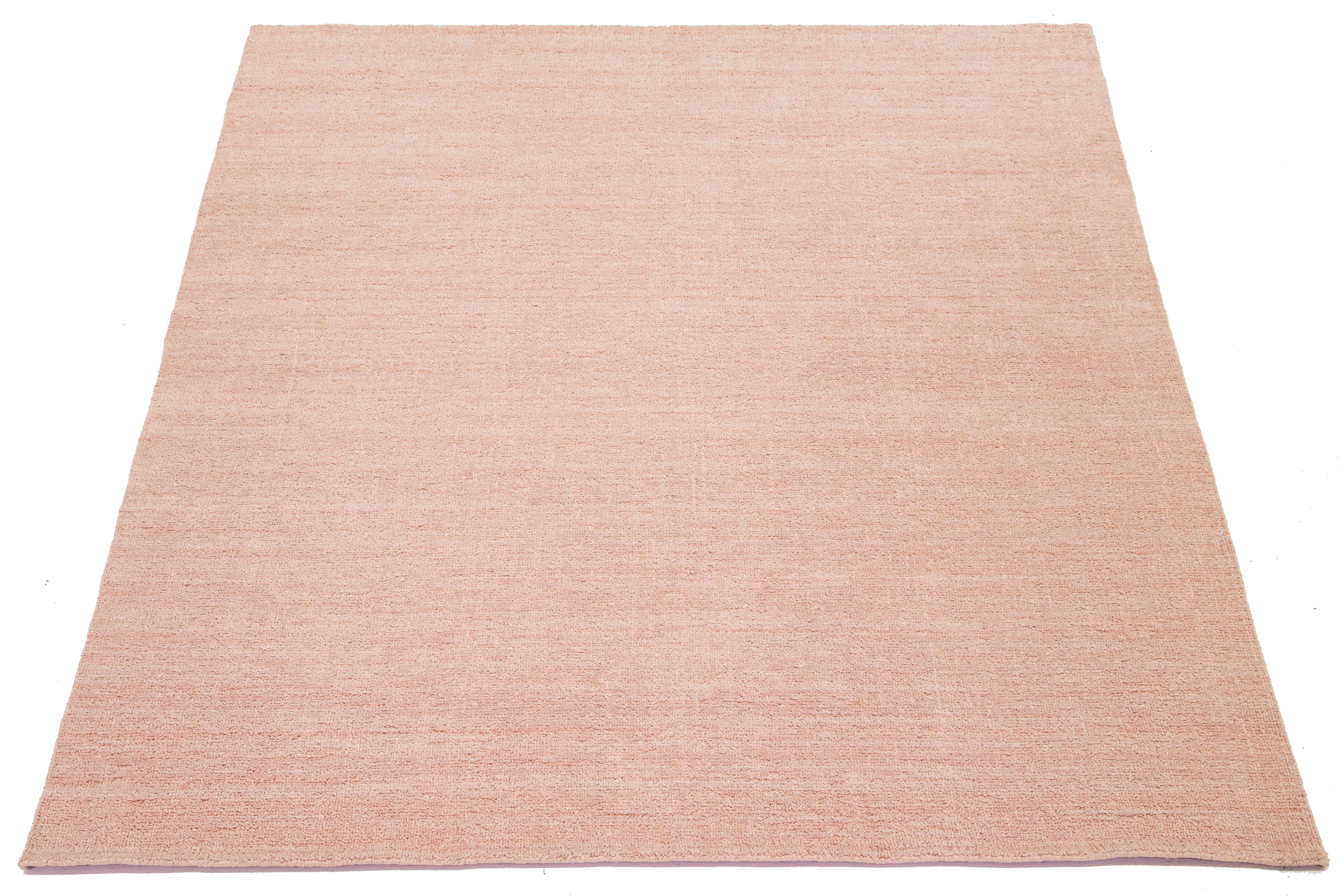 Esta moderna alfombra india de lana anudada a mano está hábilmente tejida por artesanos y presenta un diseño sólido. Su suave tono rosa sirve de fondo versátil, lo que le permite combinar a la perfección con varios estilos de interior, desde el