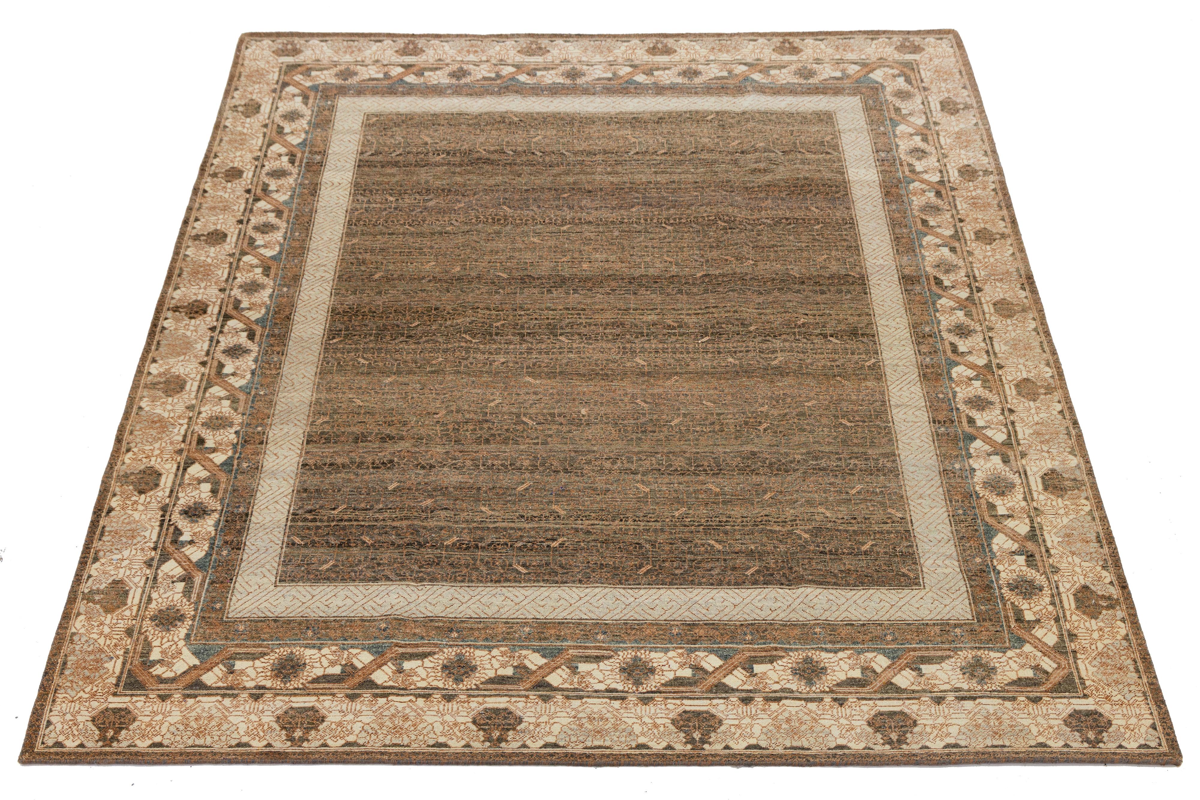 Ce tapis en laine noué à la main dans le style Khotan présente un fond marron chaud joliment rehaussé de touches de beige, d'orange et de bleu. Son design présente un motif complexe d'emboîtement sur tout le pourtour, mêlant harmonieusement des