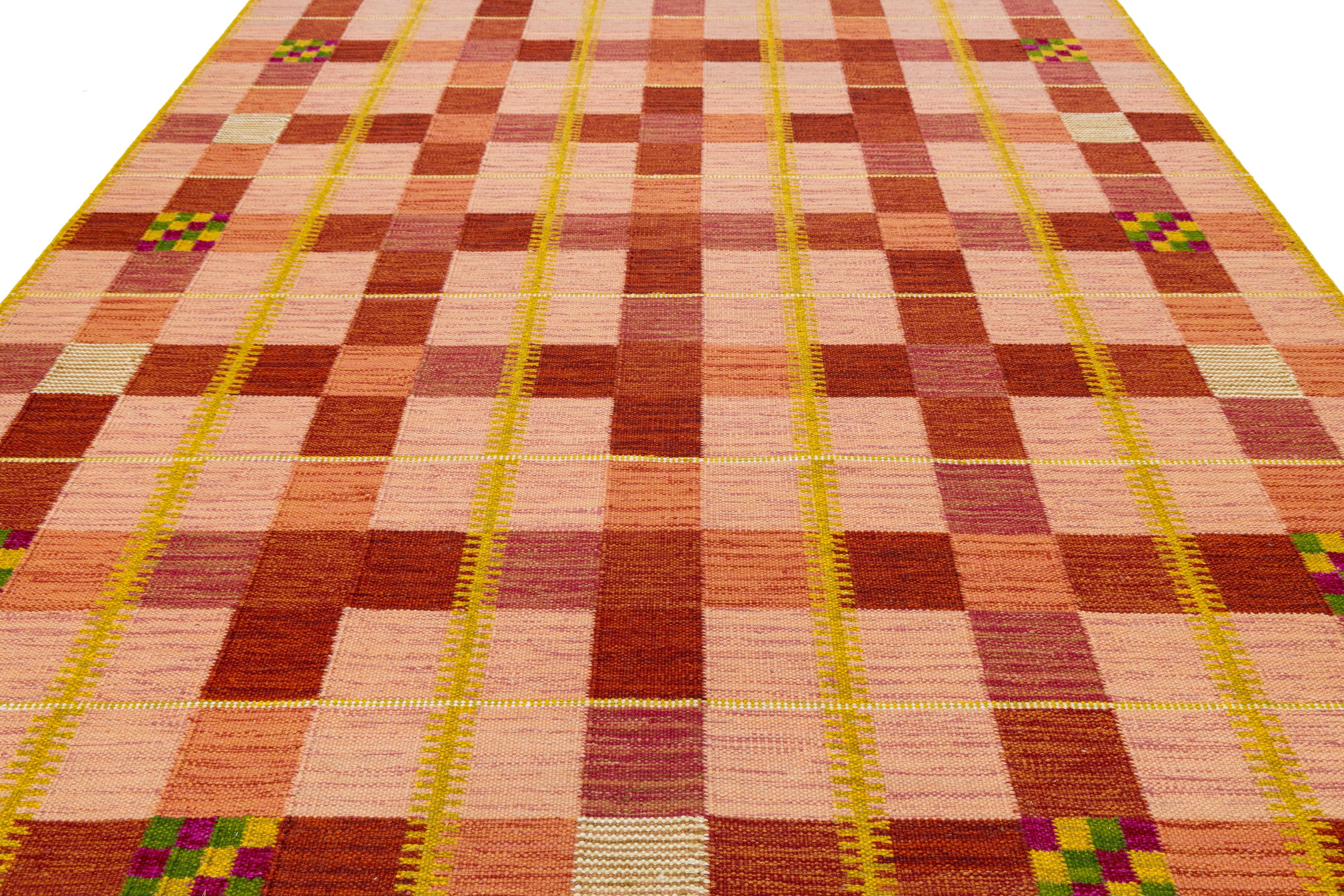 Moderner flachgewebter Wollteppich im schwedischen Stil mit einem rhythmischen Raster aus warmen Rot-, Rosa- und Orangetönen, unterbrochen von vertikalen gelben Streifen und verspielten grün-rosa Akzentquadraten. Eine kühne, geometrische Komposition