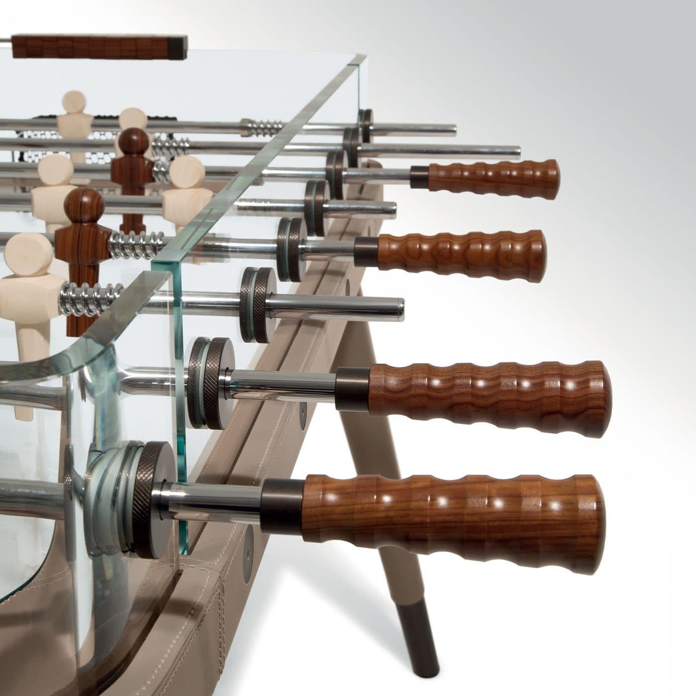 Discover this table football with tub and curved sides made of extra-clear glass. This unique table soccer features wooden legs and frame, covered in leather. The knobs are made of pau ferro and the players are made of pau iron and ash
