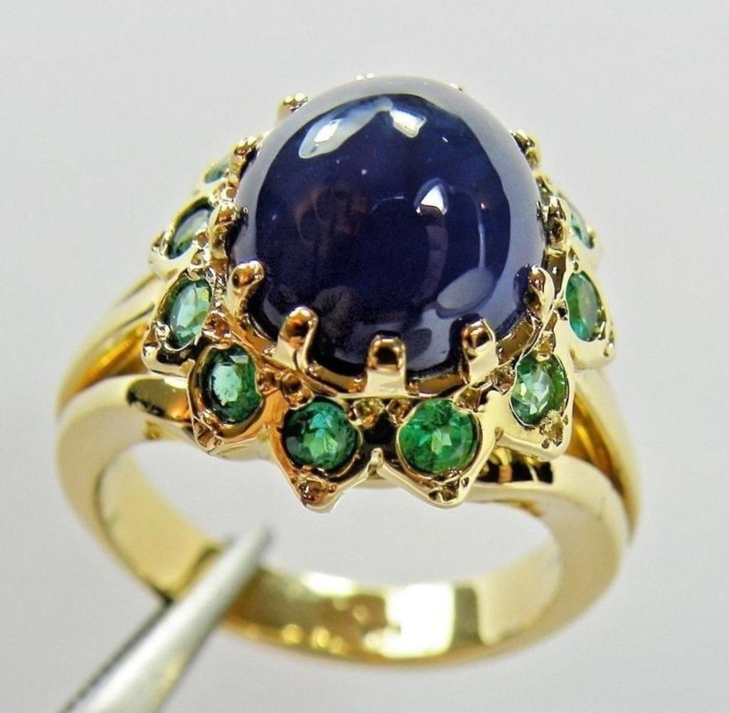This dazzling 18K yellow gold sapphire emerald ring is centered with a cabochon cut blue Burmese Sapphire, that weighs 7.75 carats. Accenting this beautiful blue sapphire are twelve round green Colombian emeralds weighing 1.25 carat. Total Ring