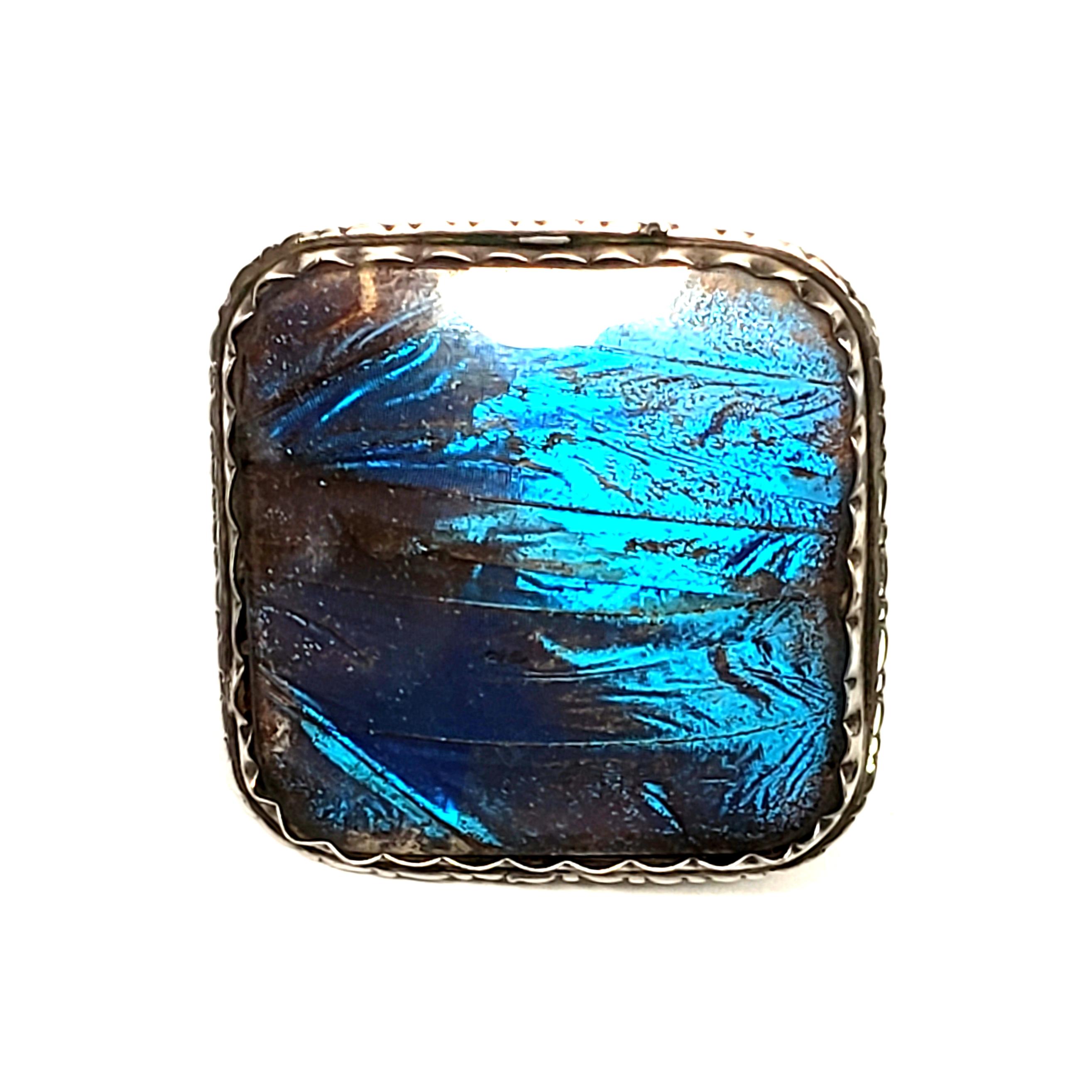 Vintage 900 silver blue butterfly wing pin by Zitrin Brasil.

Beautiful iridescent blue butterfly wing under clear dome, bezel set in square 900 silver frame.

Measures approx 1 3/8
